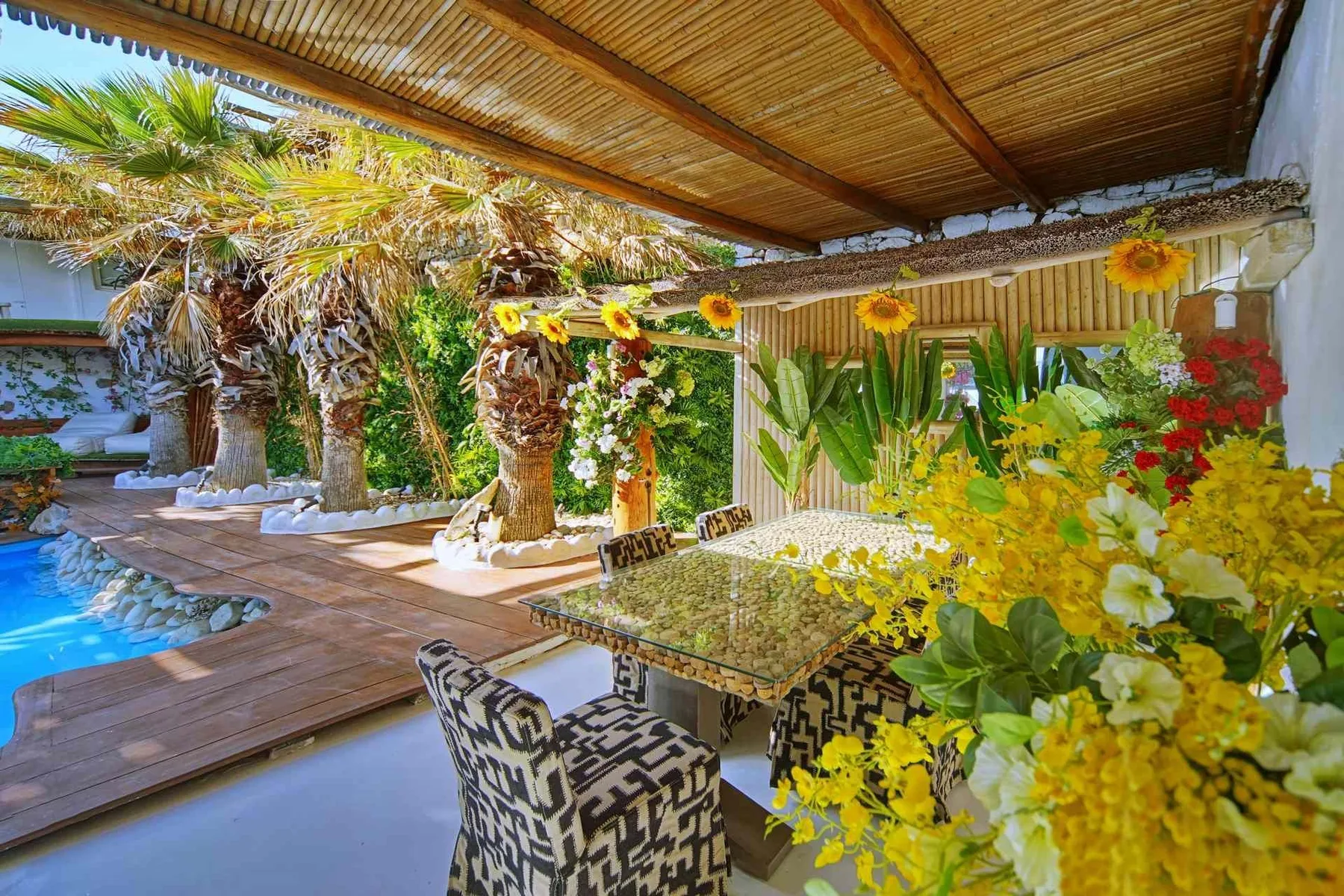 A covered outdoor dining area overlooks a swimming pool and lush garden.