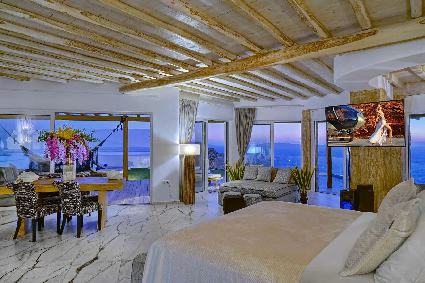 A bright bedroom and sitting area open onto ocean views through large windows.