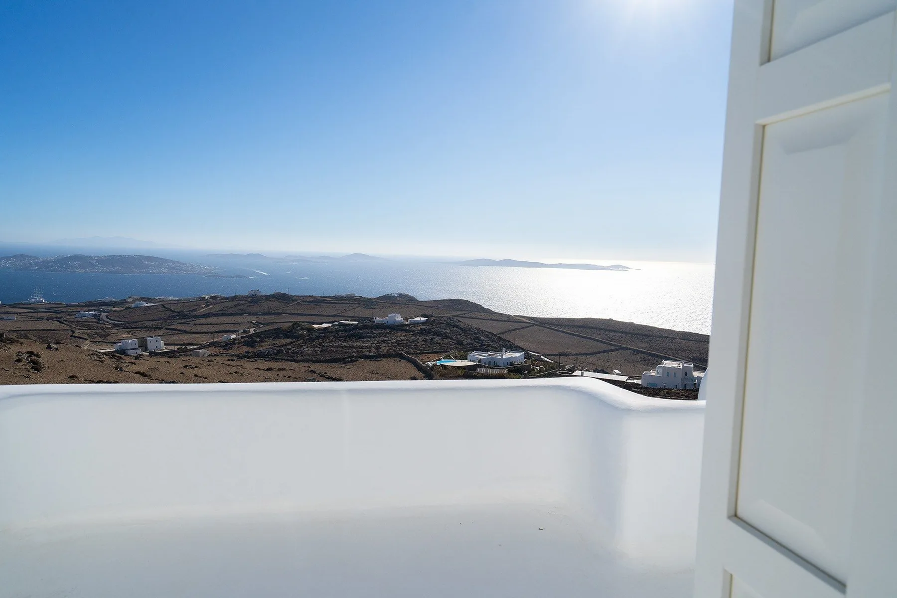 A white balcony overlooks a coastal landscape and the sea.