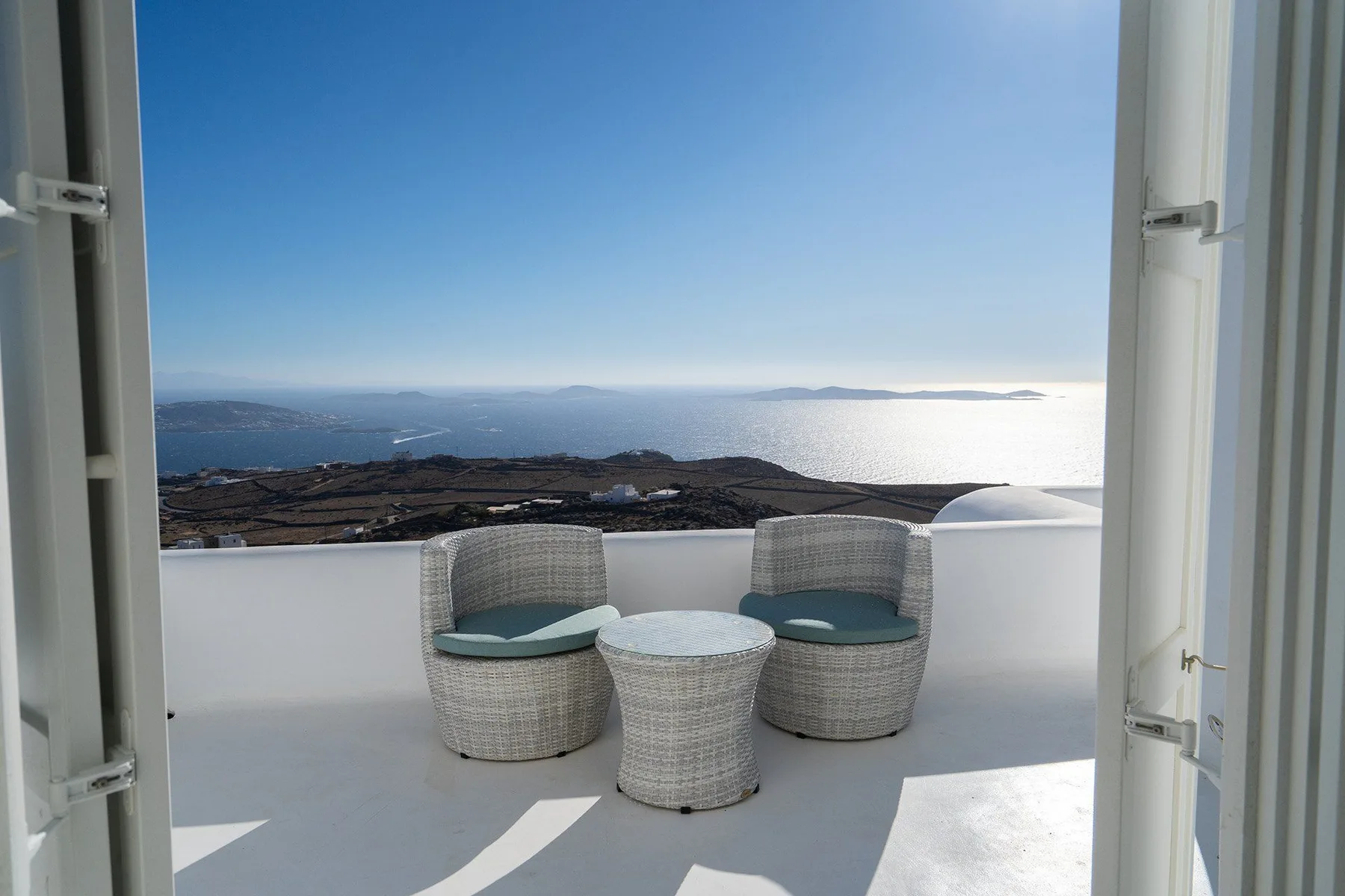 A bright terrace with woven seating overlooks the sea and distant islands.