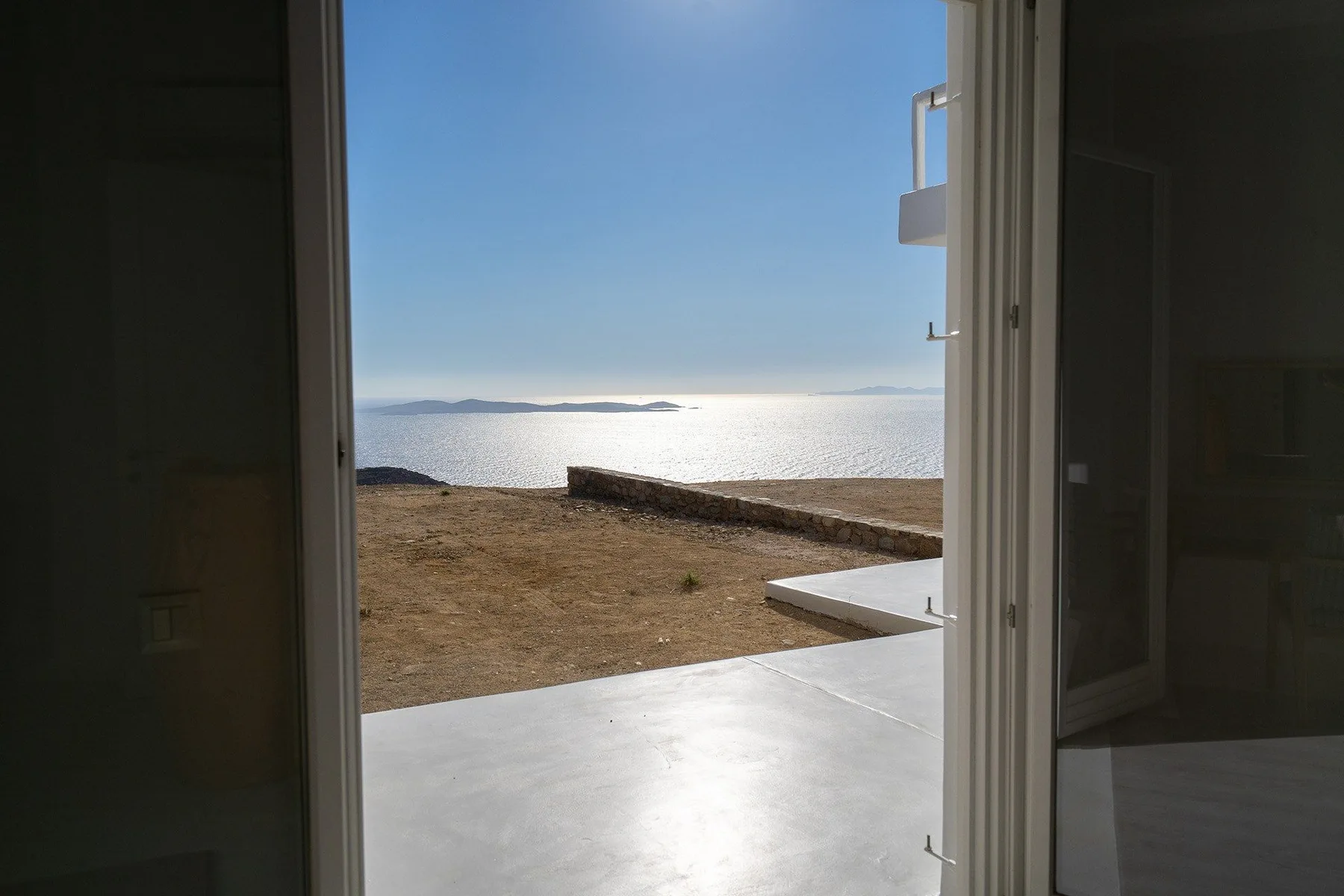 An open doorway looks out onto a bright seaside terrace and calm water.