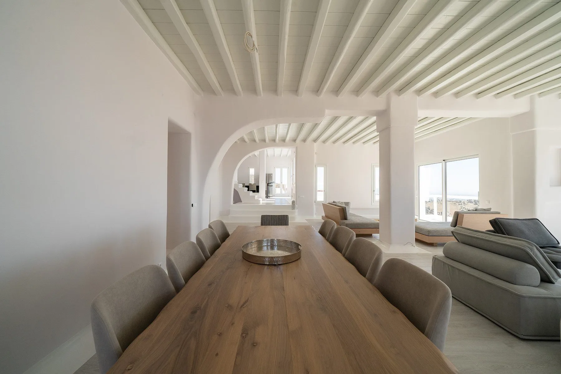 A bright dining area with a long wooden table and seating beneath exposed ceiling beams.