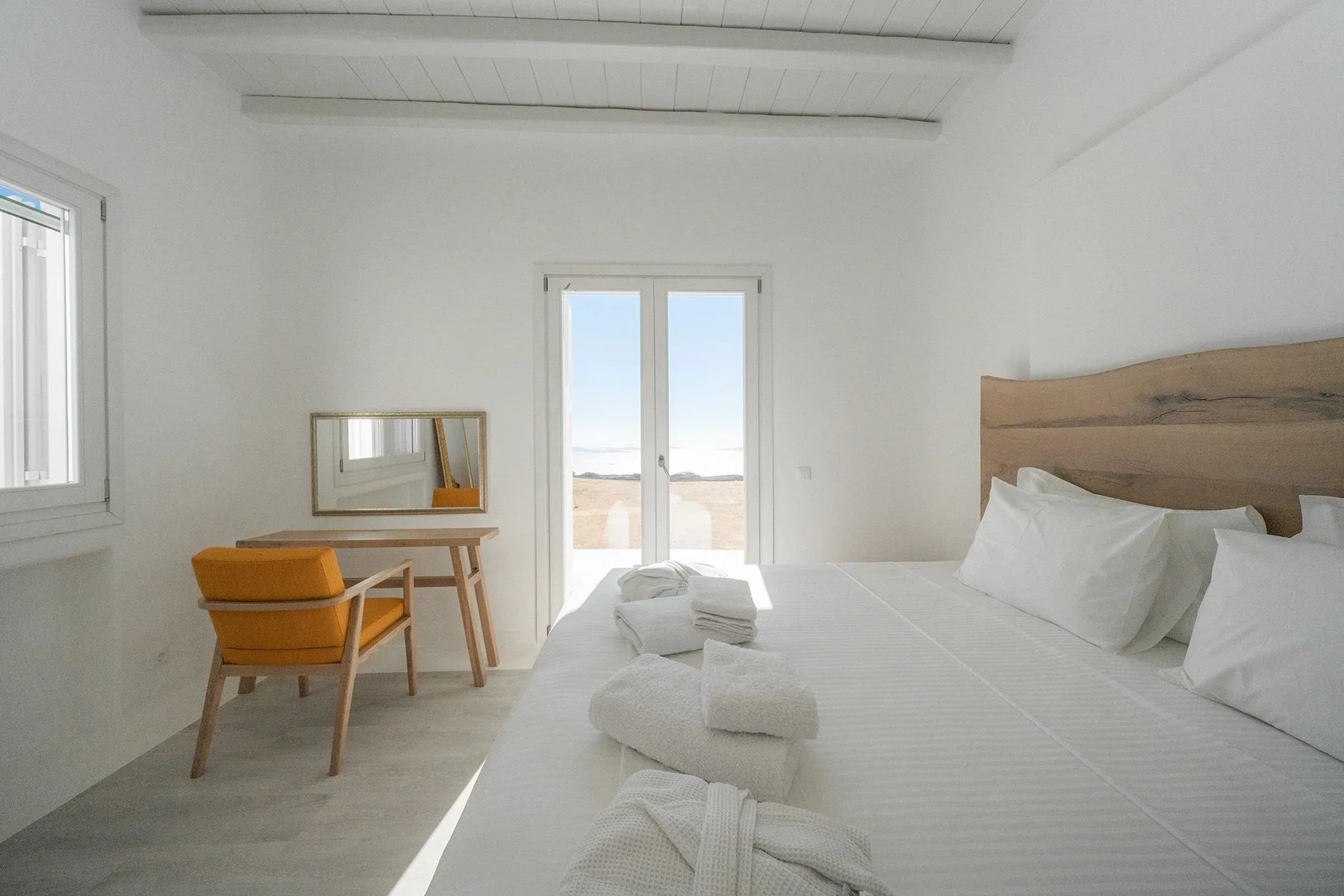 A bright bedroom with a large bed, a desk, and windows overlooking the coast.