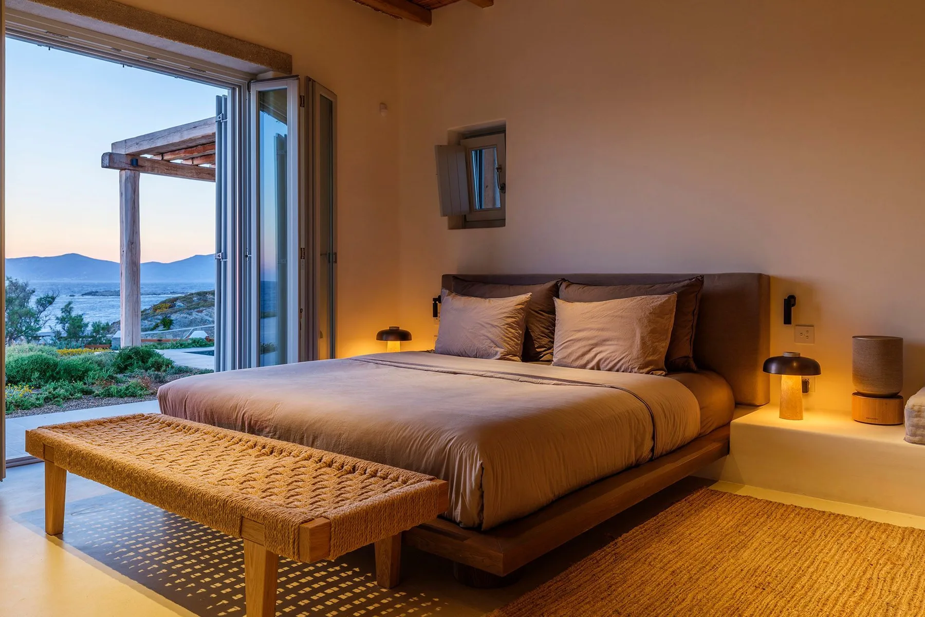 A bedroom with a neatly made bed and an open doorway overlooking the landscape.