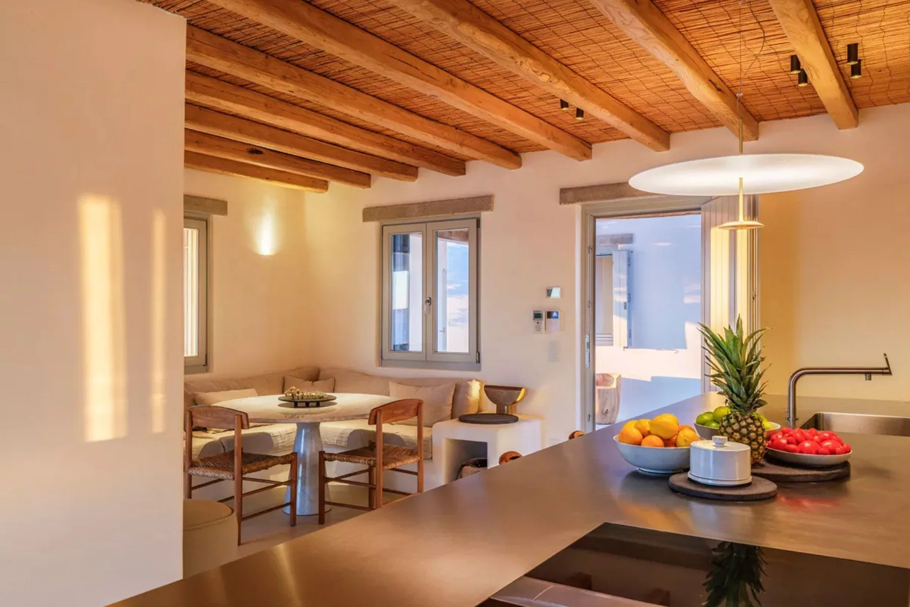 A warm open-plan kitchen and dining area with wooden ceiling beams and a table.