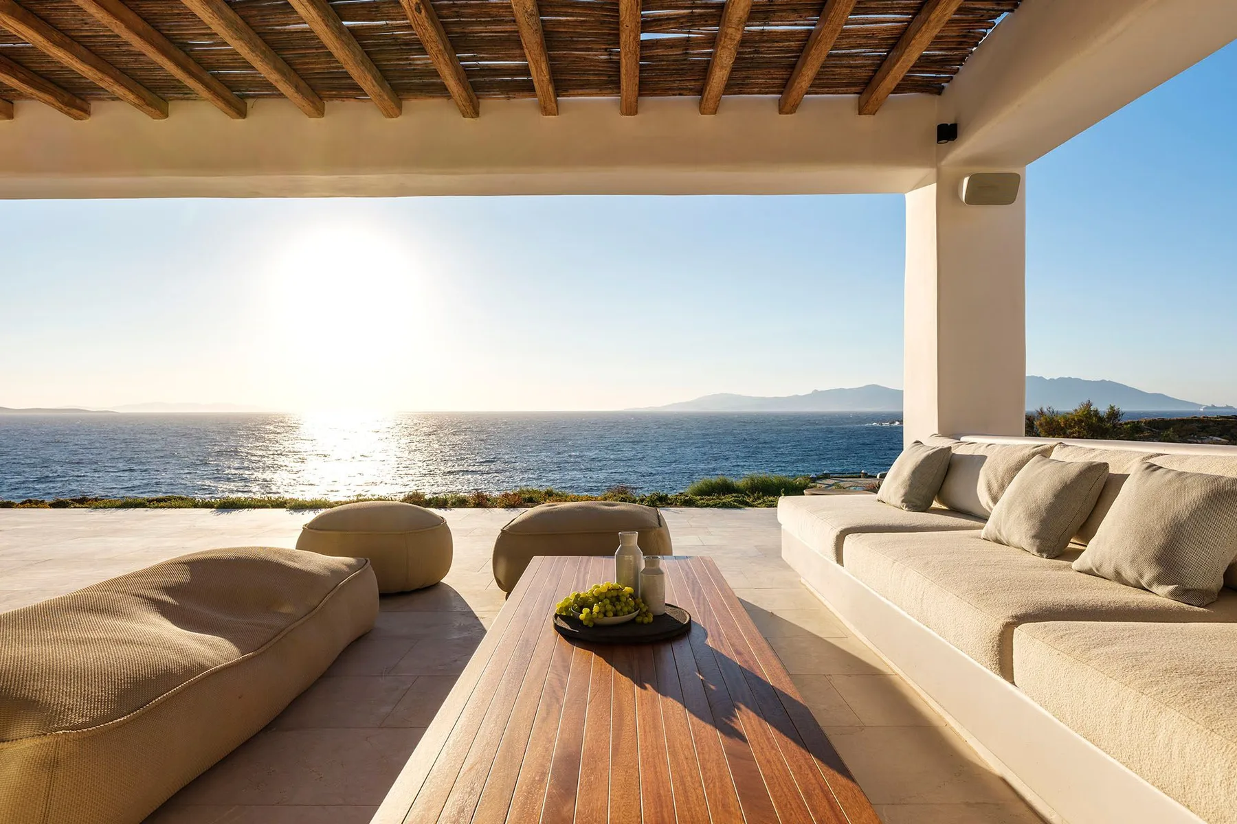A covered outdoor lounge with cushioned seating and a view of the sea.