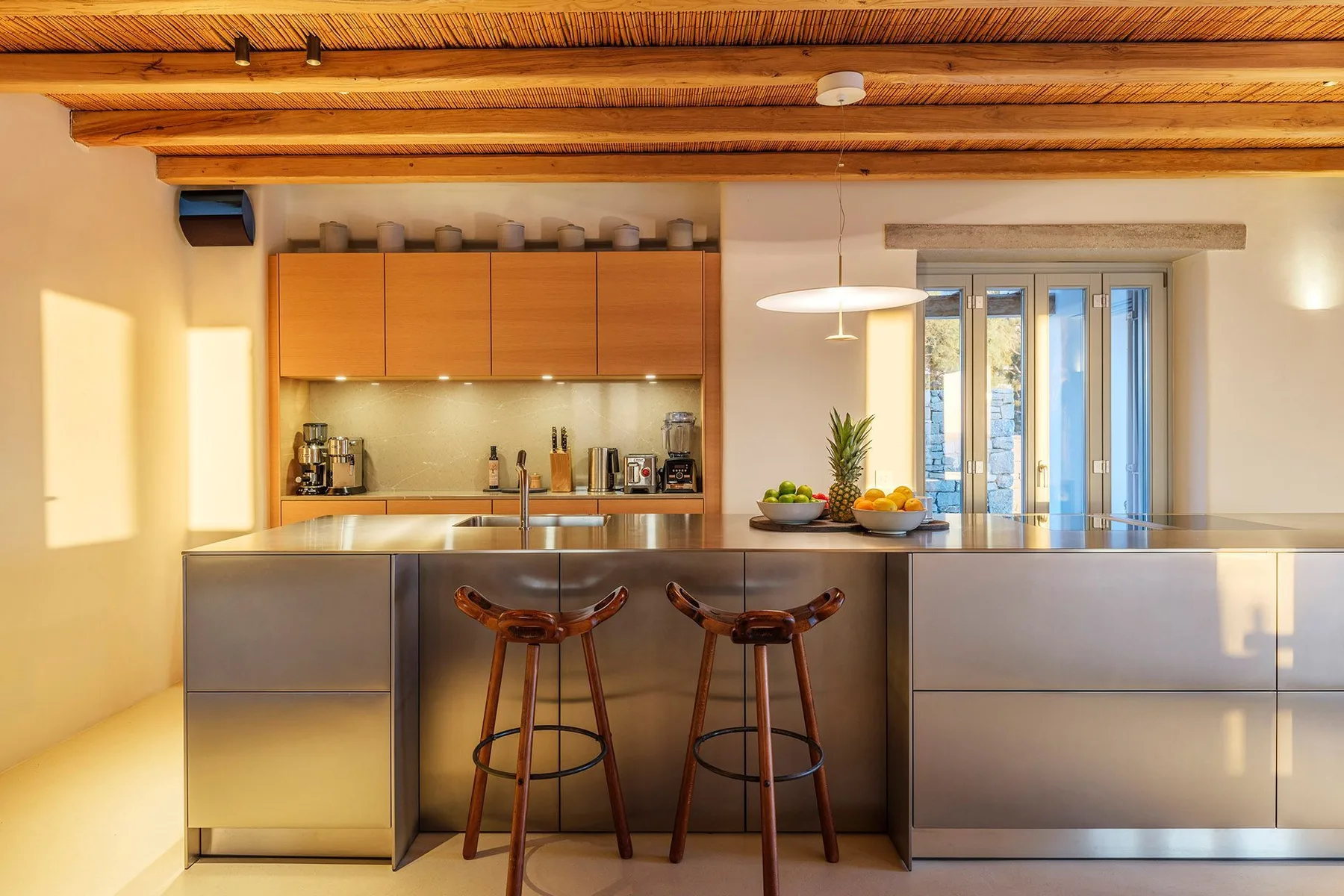A modern kitchen with a counter, two stools, and large windows.