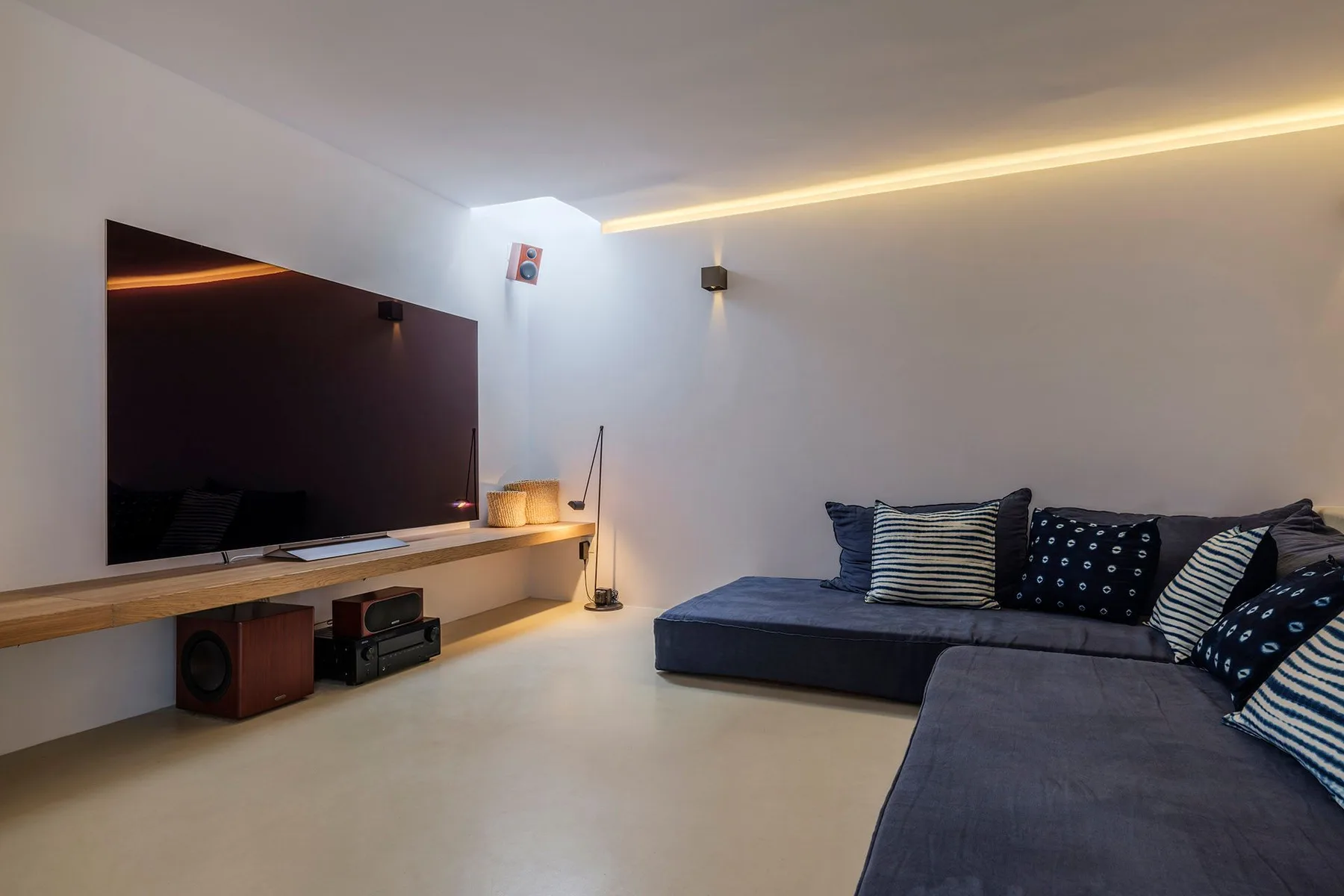 A living room with a television on a wall shelf and dark seating.