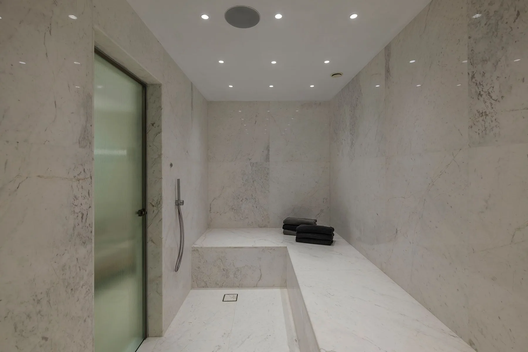 A marble-tiled bathroom with a walk-in shower and a glass door.