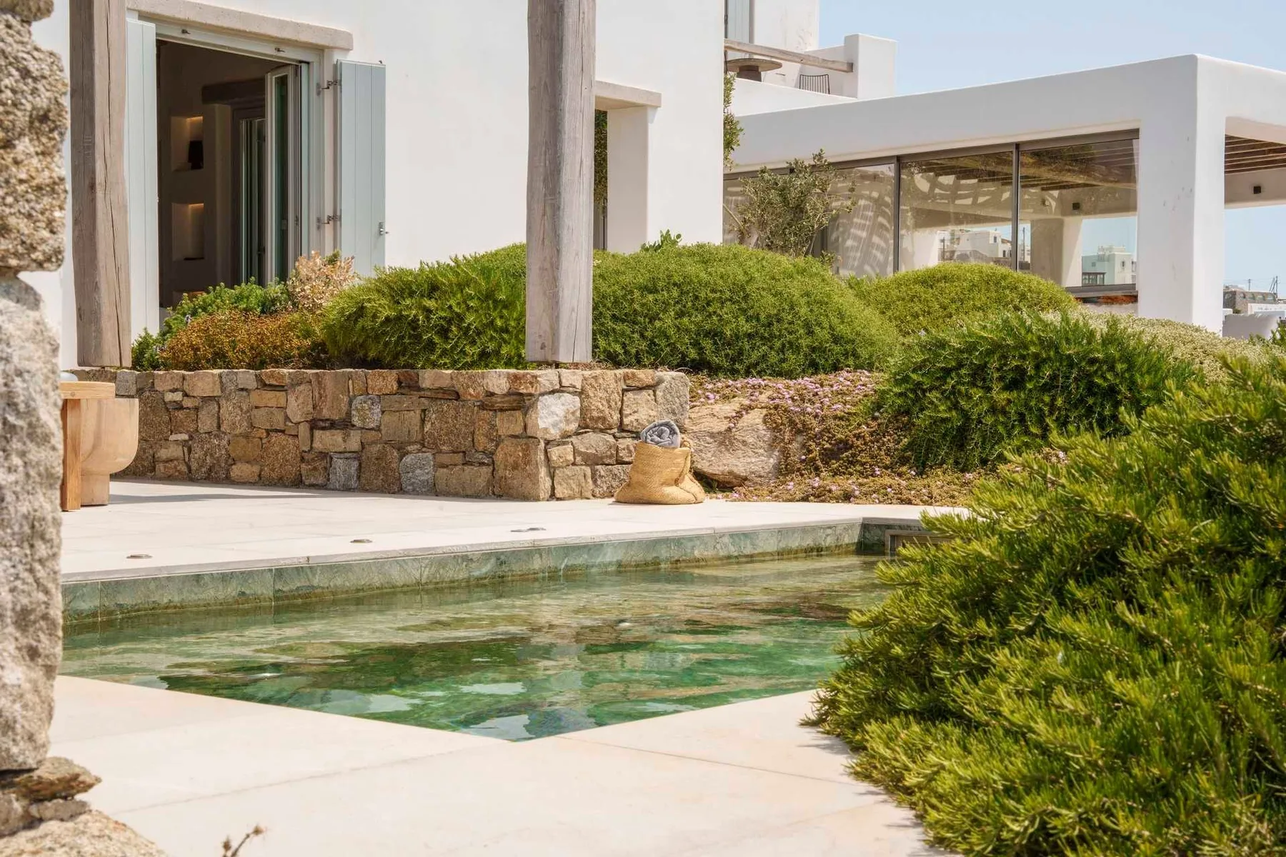 A small outdoor pool sits beside a white building and green shrubs.
