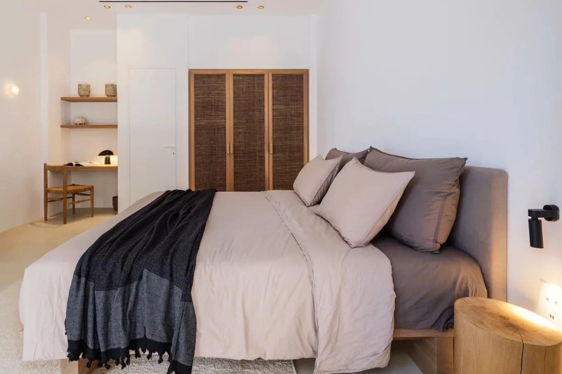 A bedroom with a neatly made bed and a dark throw blanket.