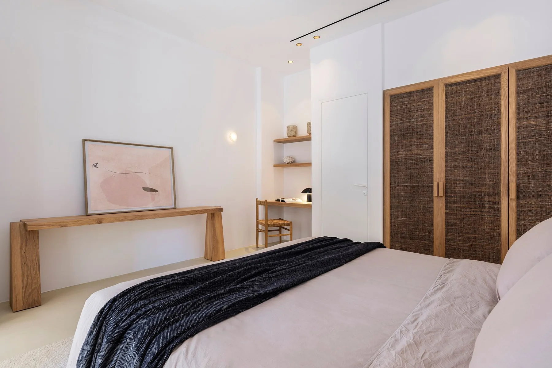 A bright bedroom with a bed, a wooden console, and woven closet doors.