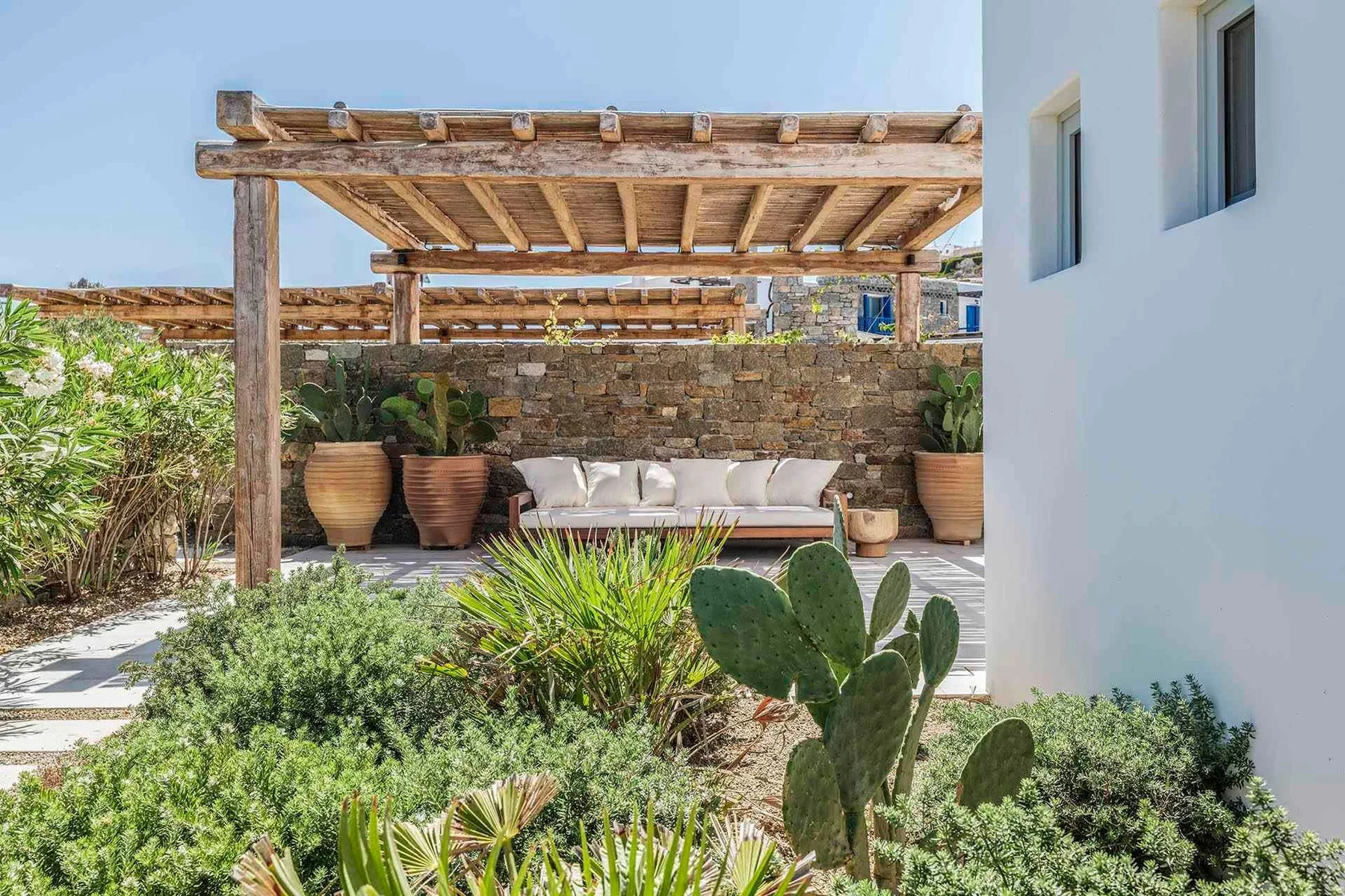 A pergola-covered outdoor seating area sits among potted plants and desert landscaping.