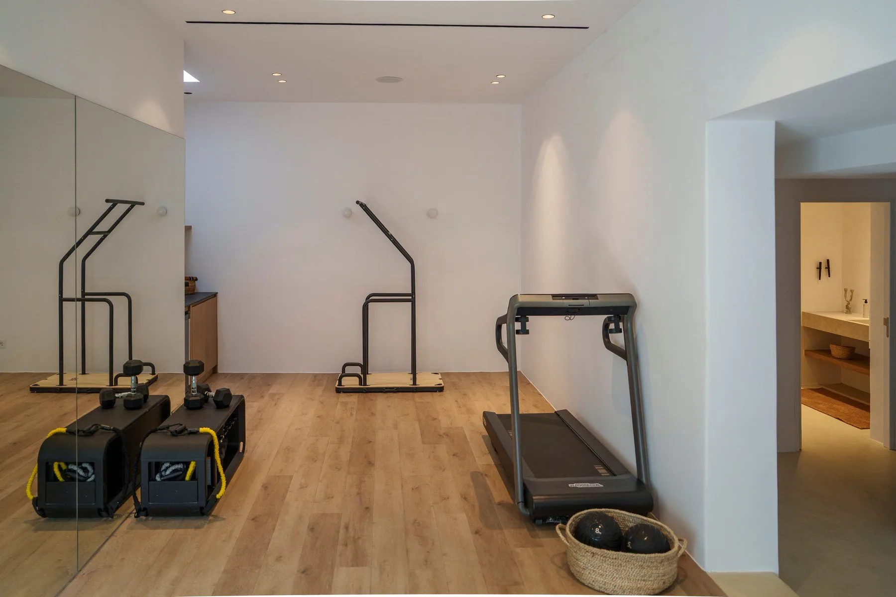 A bright home gym with exercise equipment and a treadmill on a wood floor.