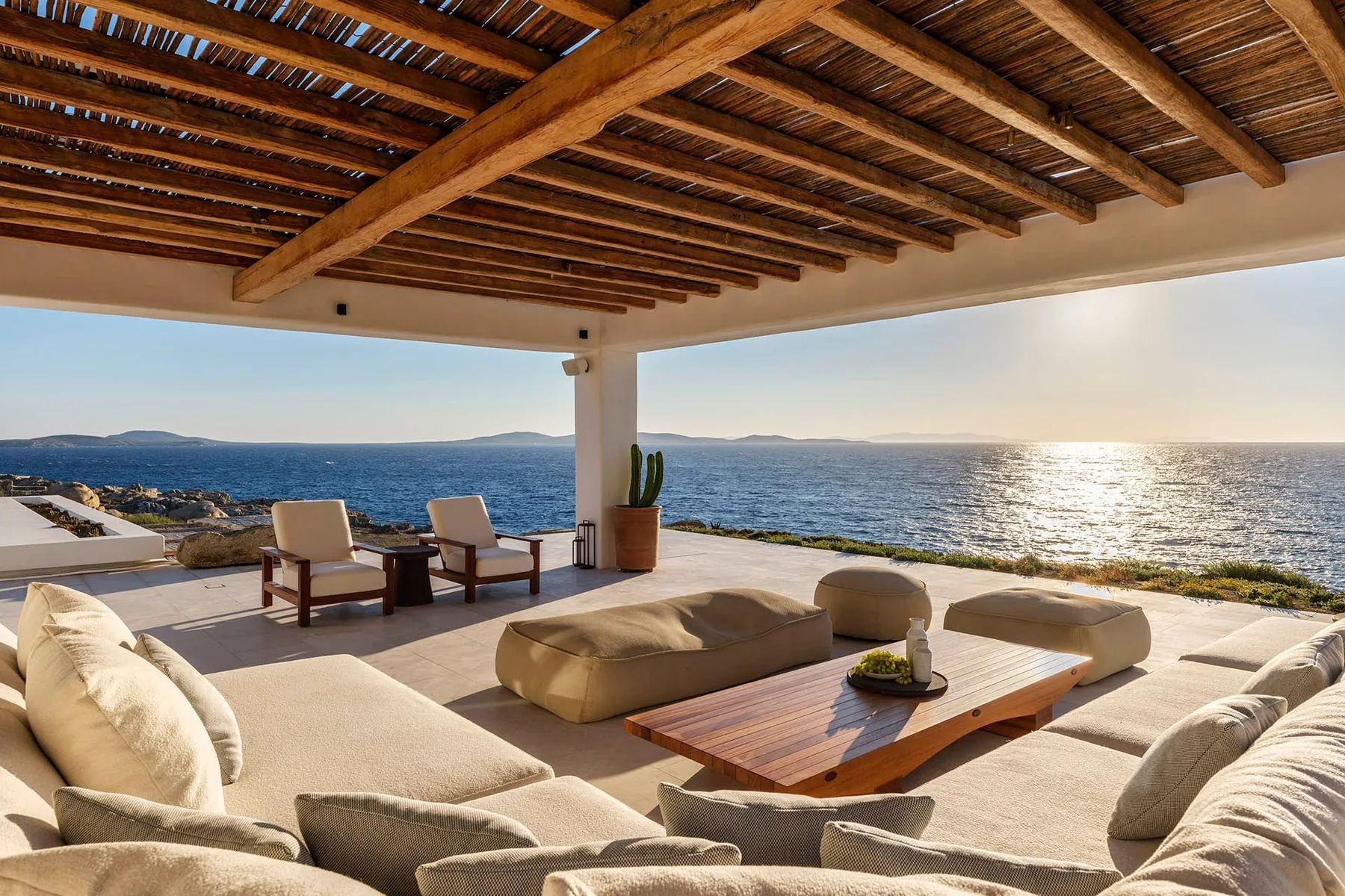 A covered seaside terrace has cushioned seating and a view across the water.