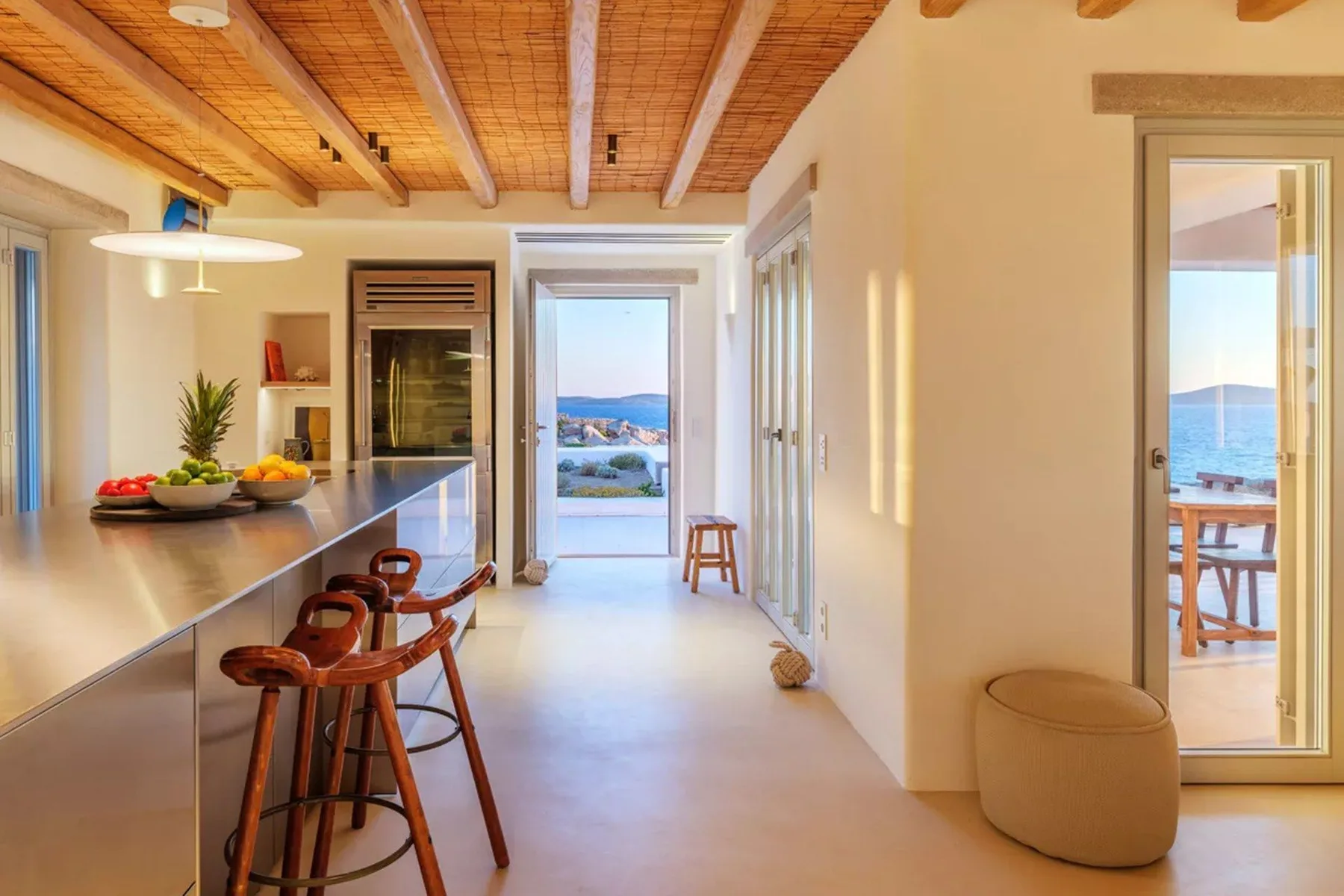 A bright open-plan kitchen and dining area with a long counter and wooden ceiling beams.