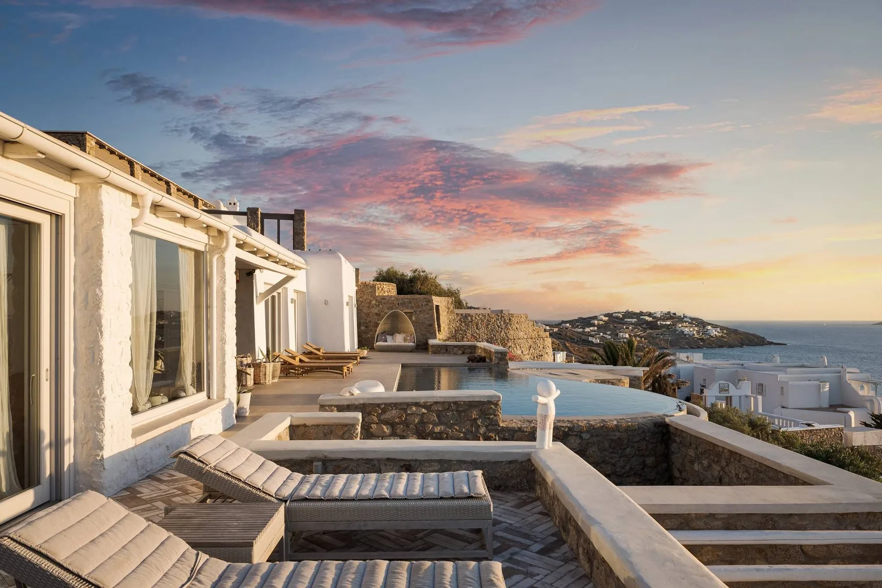 Una terraza con asientos y piscina contempla la costa al atardecer.