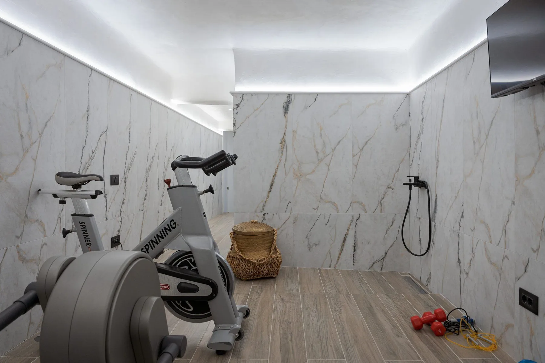 Un gimnasio con bicicletas estáticas, pesas y un televisor en la pared.