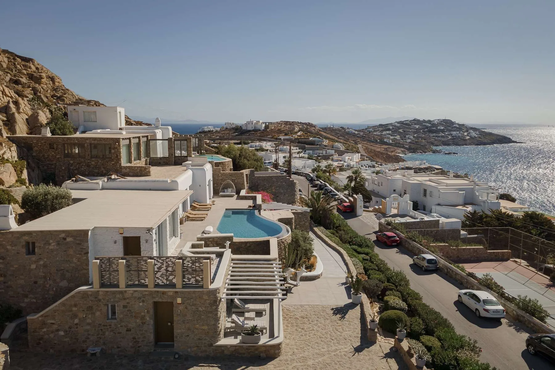 Viviendas en una ladera costera miran al mar, con una piscina junto a un edificio de piedra.