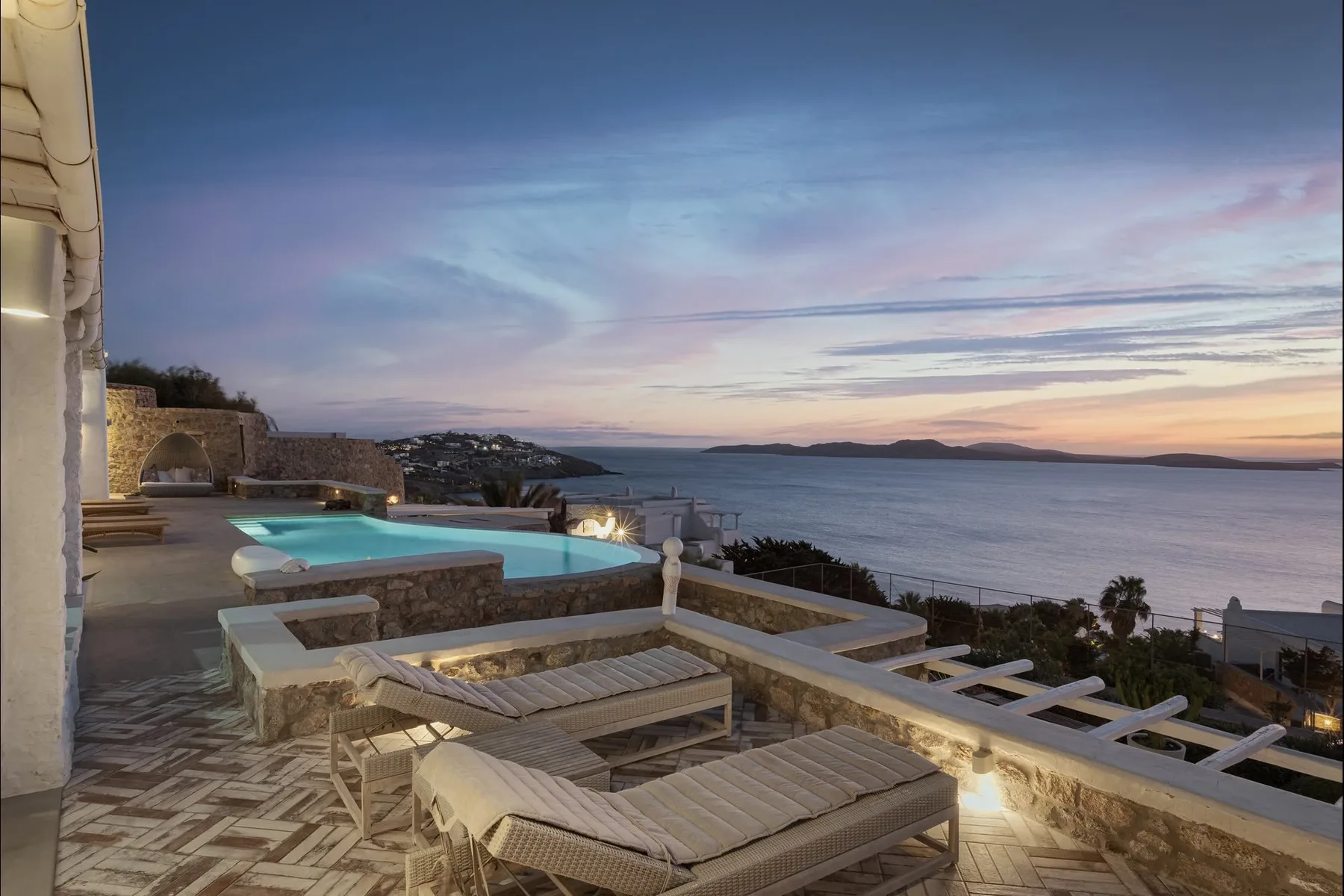 Una terraza junto al mar con asientos y una piscina ofrece vistas al agua al anochecer.