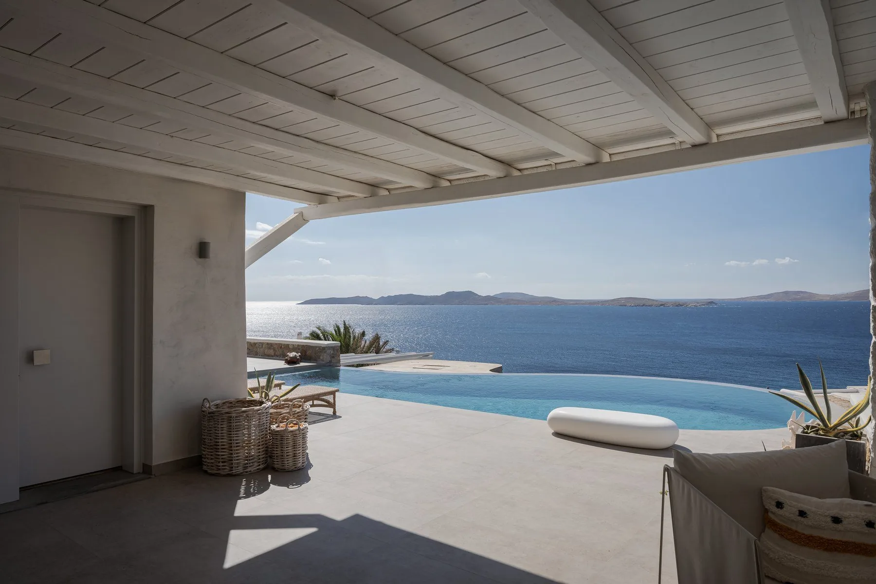 Un patio cubierto da a una piscina y a una amplia vista al mar.