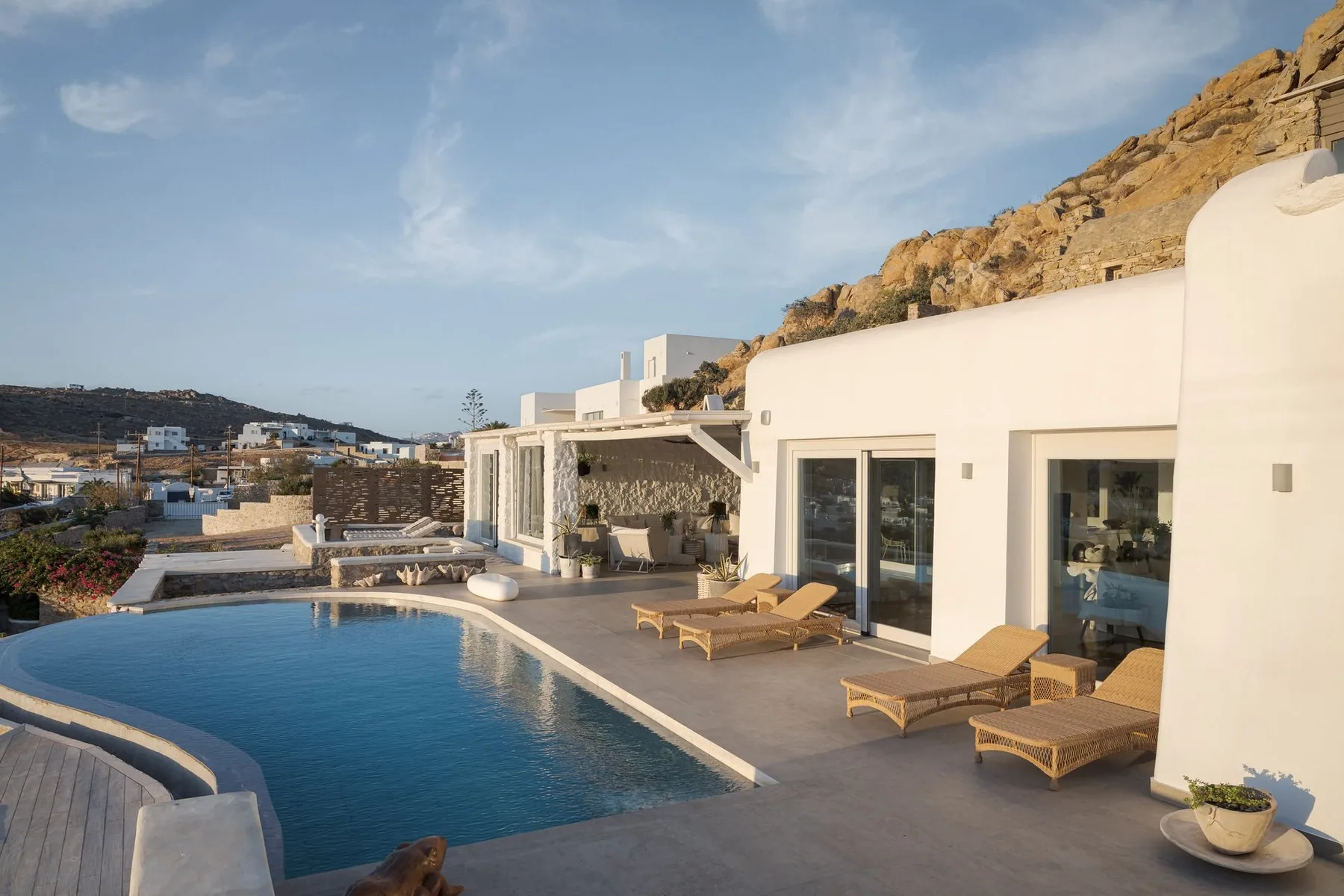 Un edificio blanco da a una piscina, con asientos de descanso en la terraza.