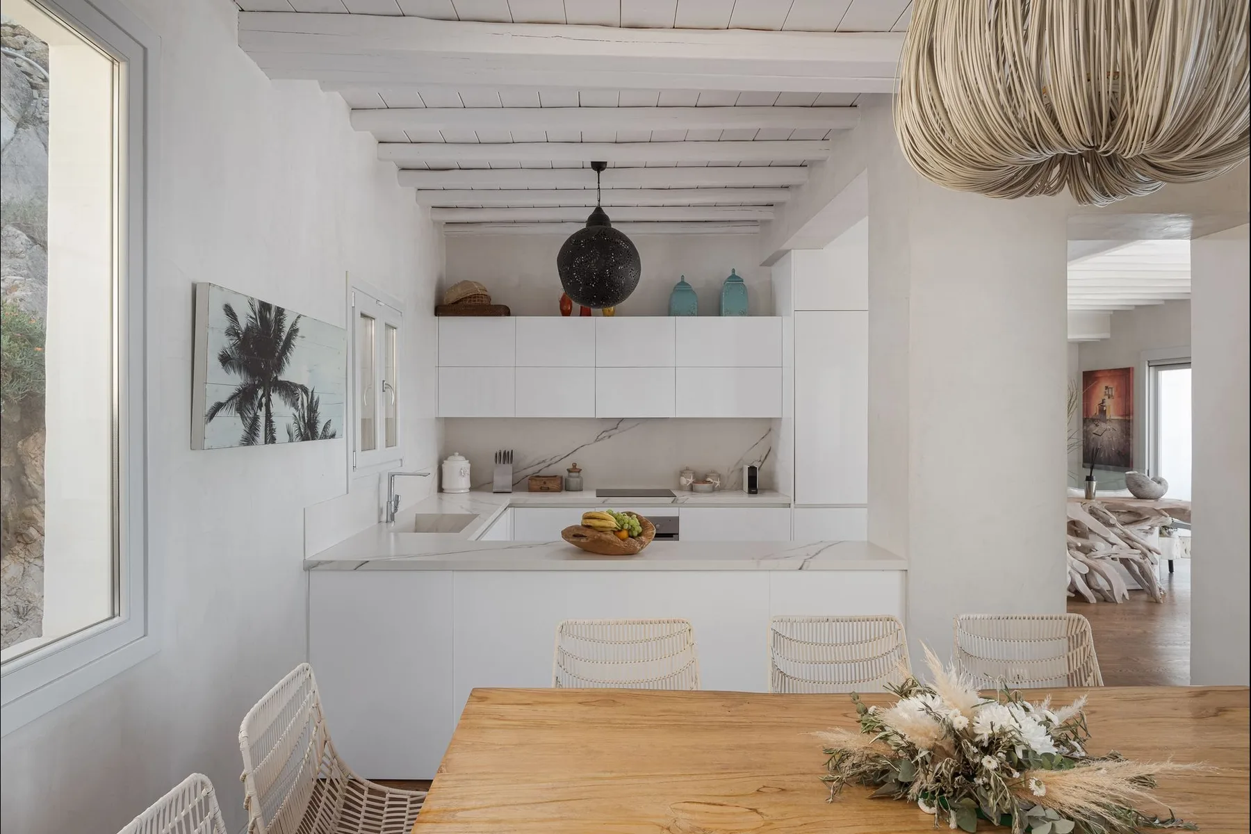 Una luminosa cocina abierta al comedor, con una mesa de madera y armarios blancos.