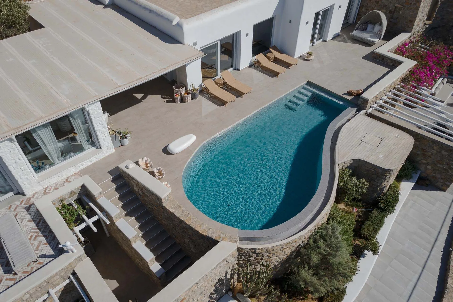 Una piscina al aire libre junto a una casa moderna y un patio pavimentado.