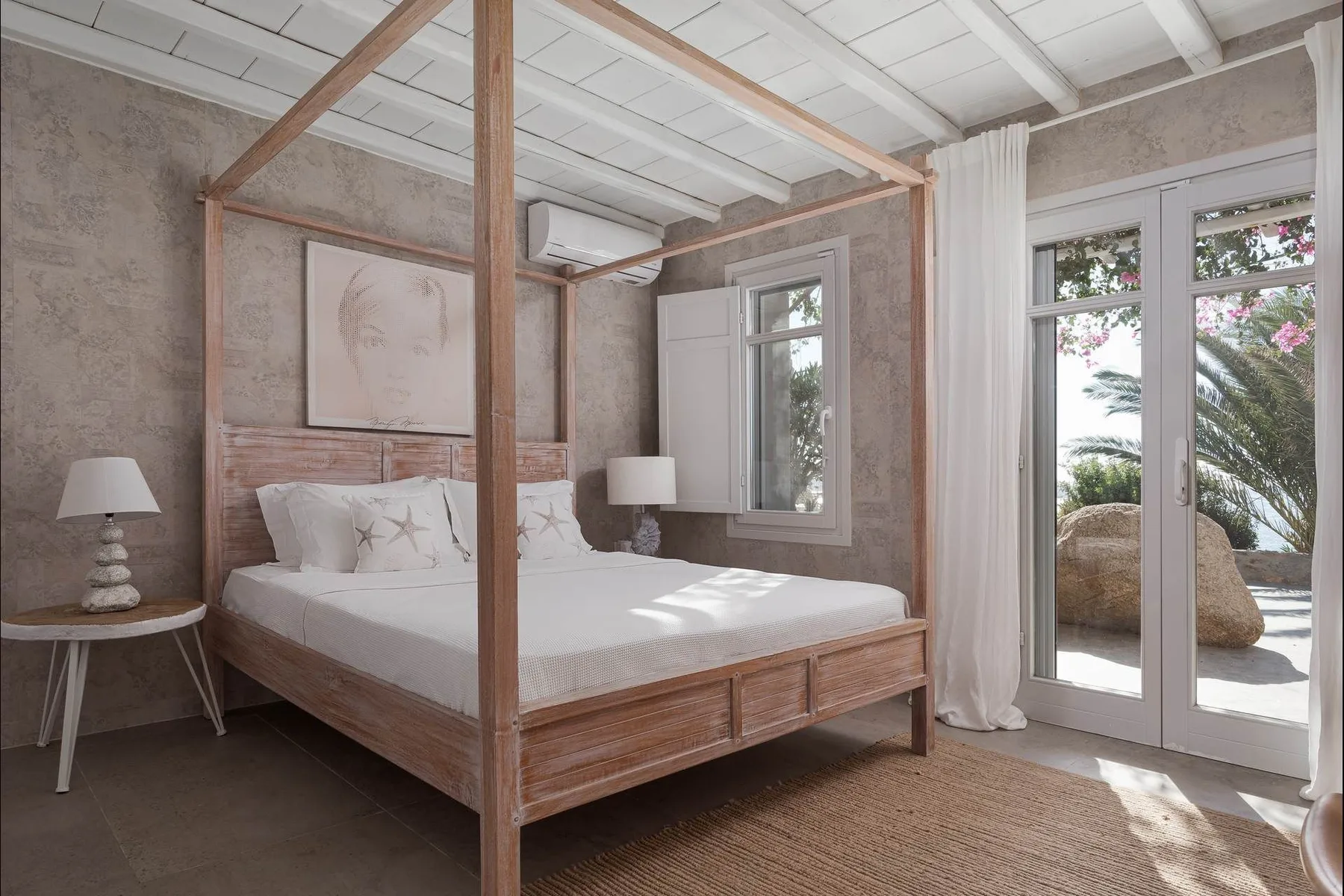 Un dormitorio con una cama con dosel de madera junto a puertas de vidrio que dan a un patio.