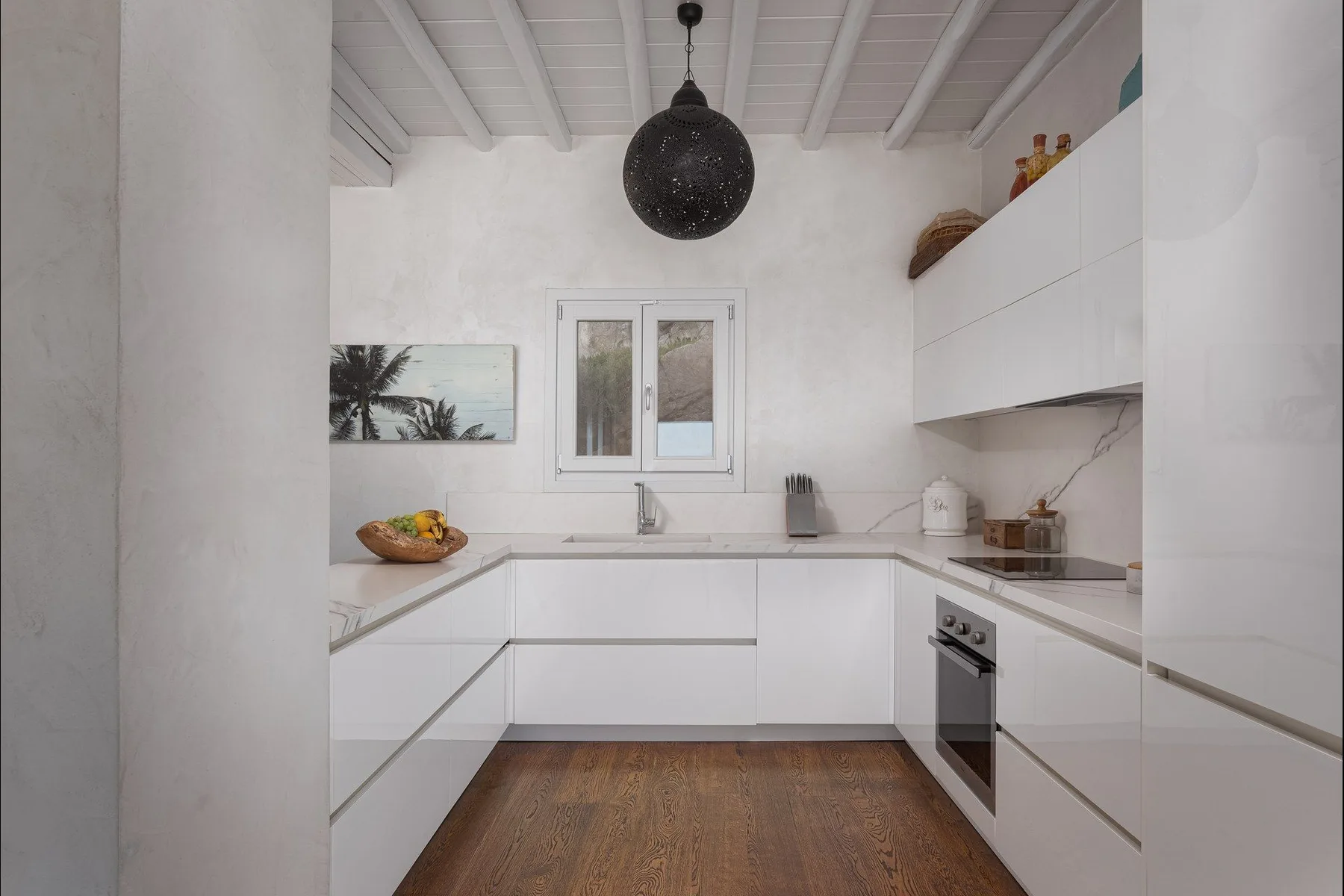 Una cocina blanca y luminosa con una ventana central y horno integrado.