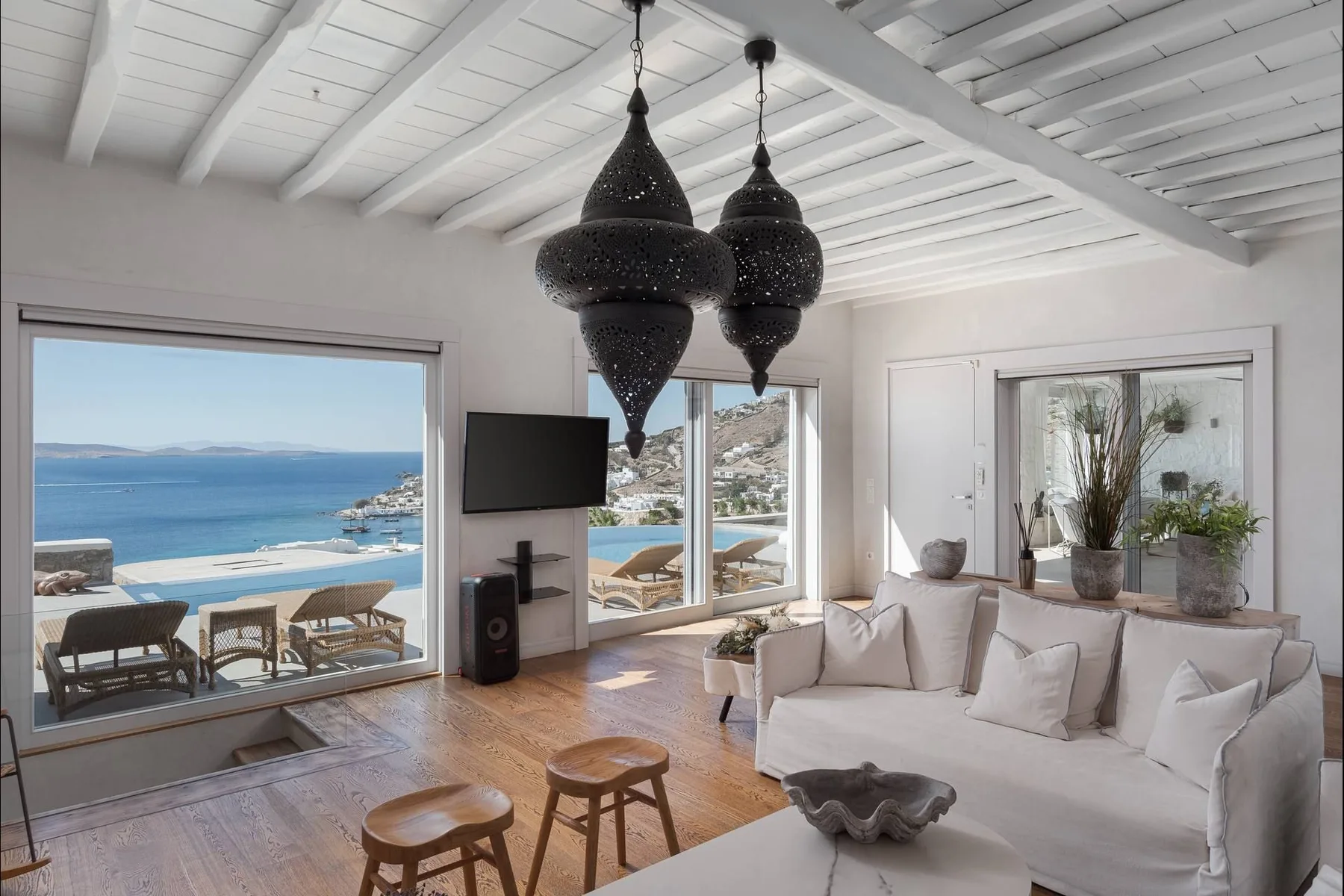 Una sala luminosa con asientos claros, lámparas colgantes oscuras y vistas al mar por amplios ventanales.