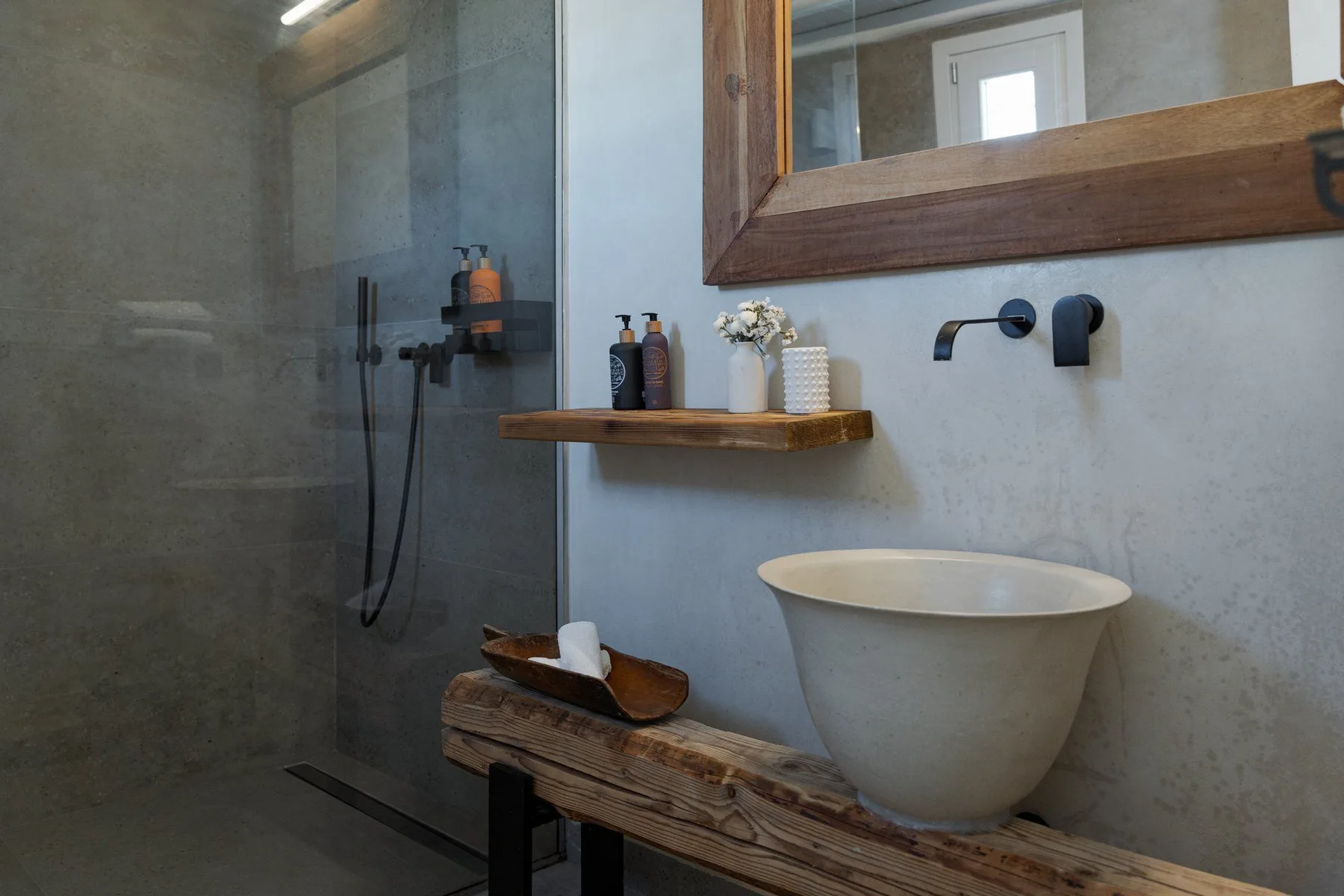 Un baño con lavabo sobre encimera, grifo de pared y ducha de vidrio.