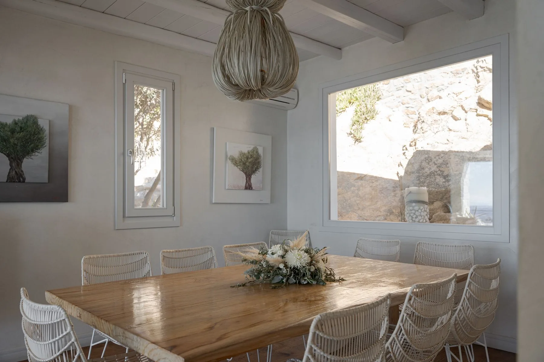 Un comedor luminoso con una mesa de madera y asientos tejidos bajo una lámpara colgante.