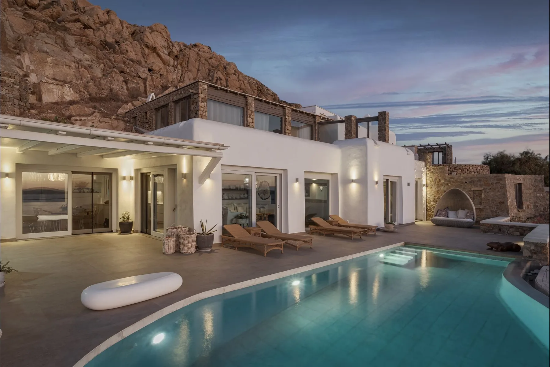 Una casa blanca moderna da a una piscina bajo una ladera rocosa.