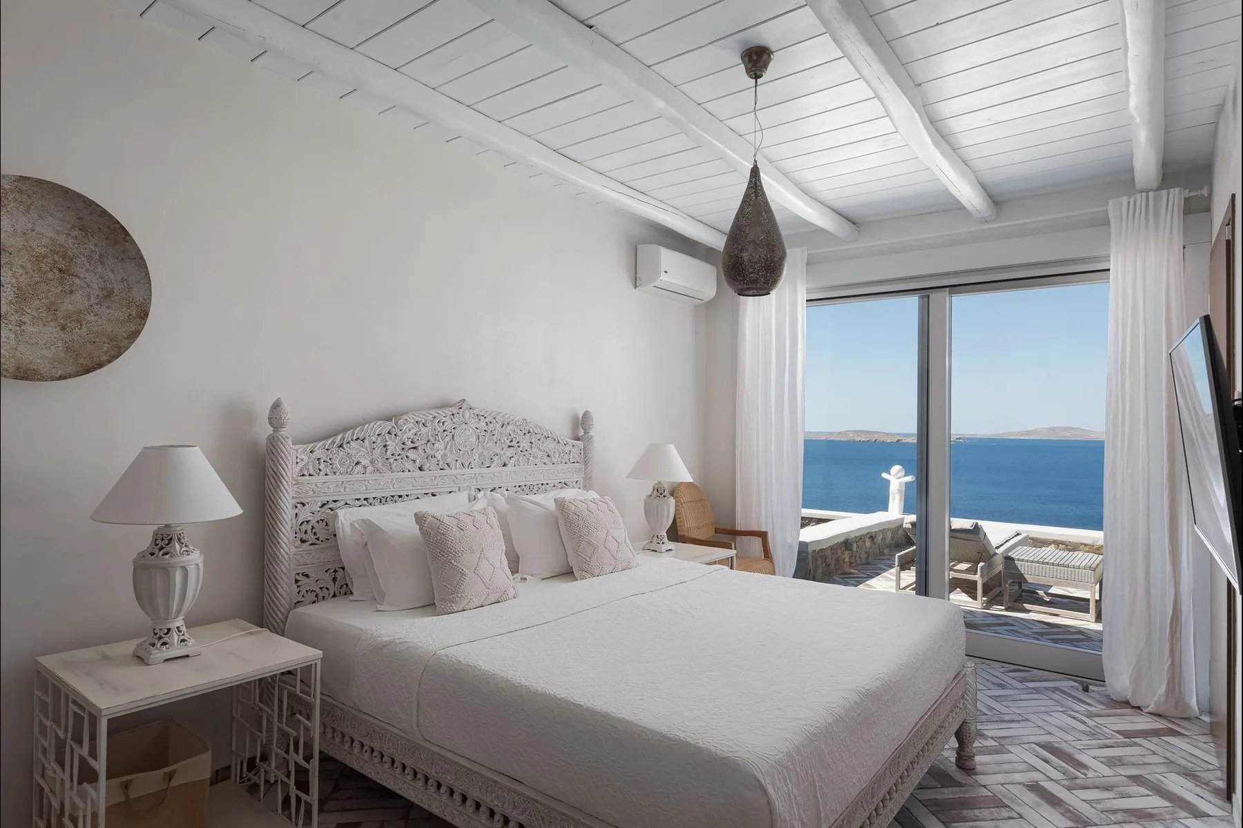 Un dormitorio luminoso con una cama grande y puertas correderas de cristal que dan al mar.