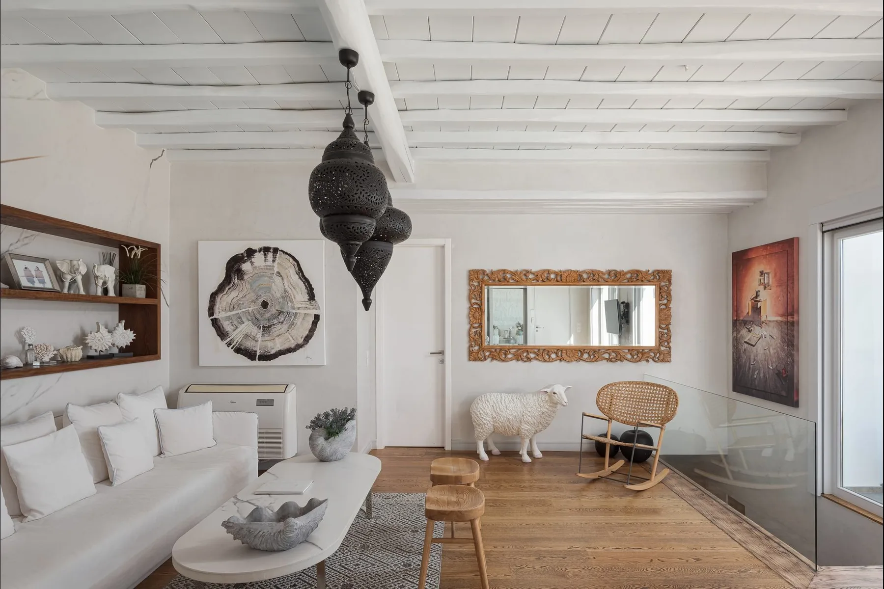 Una sala luminosa con asientos blancos, suelo de madera y un gran espejo en la pared.