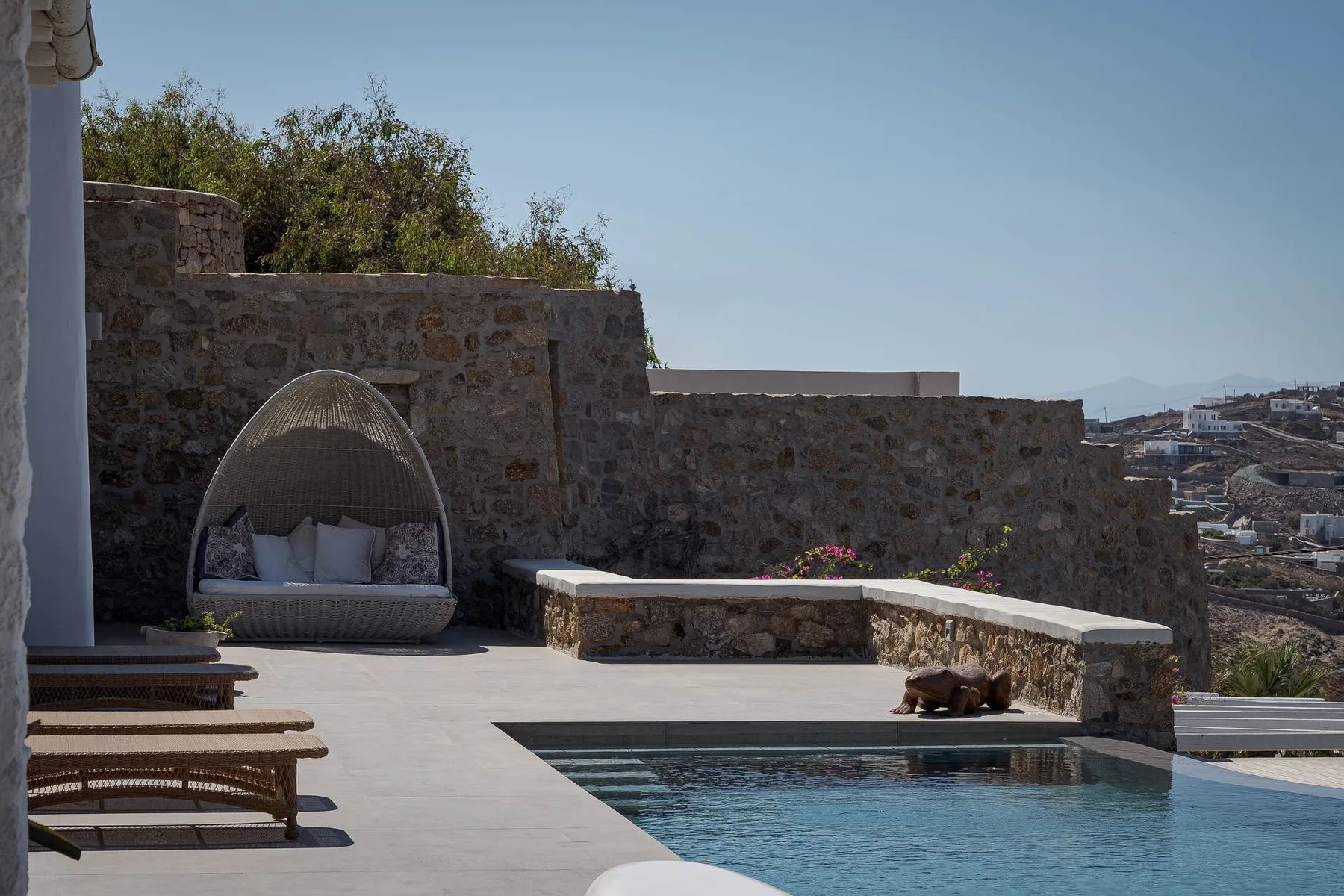 Una terraza junto a la piscina, con un asiento acolchado y muros de piedra, da a las colinas.