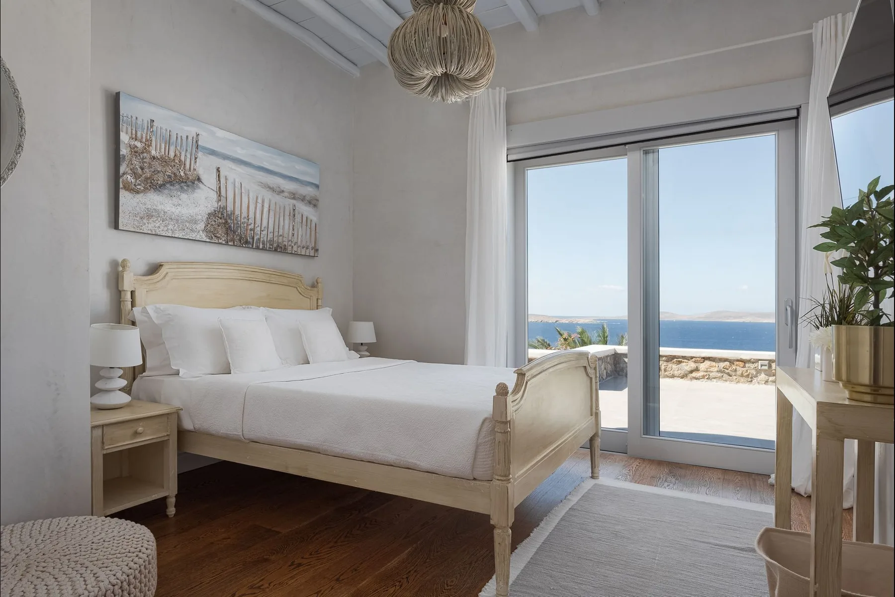 Un dormitorio luminoso con una cama frente a grandes puertas de cristal y vistas al mar.
