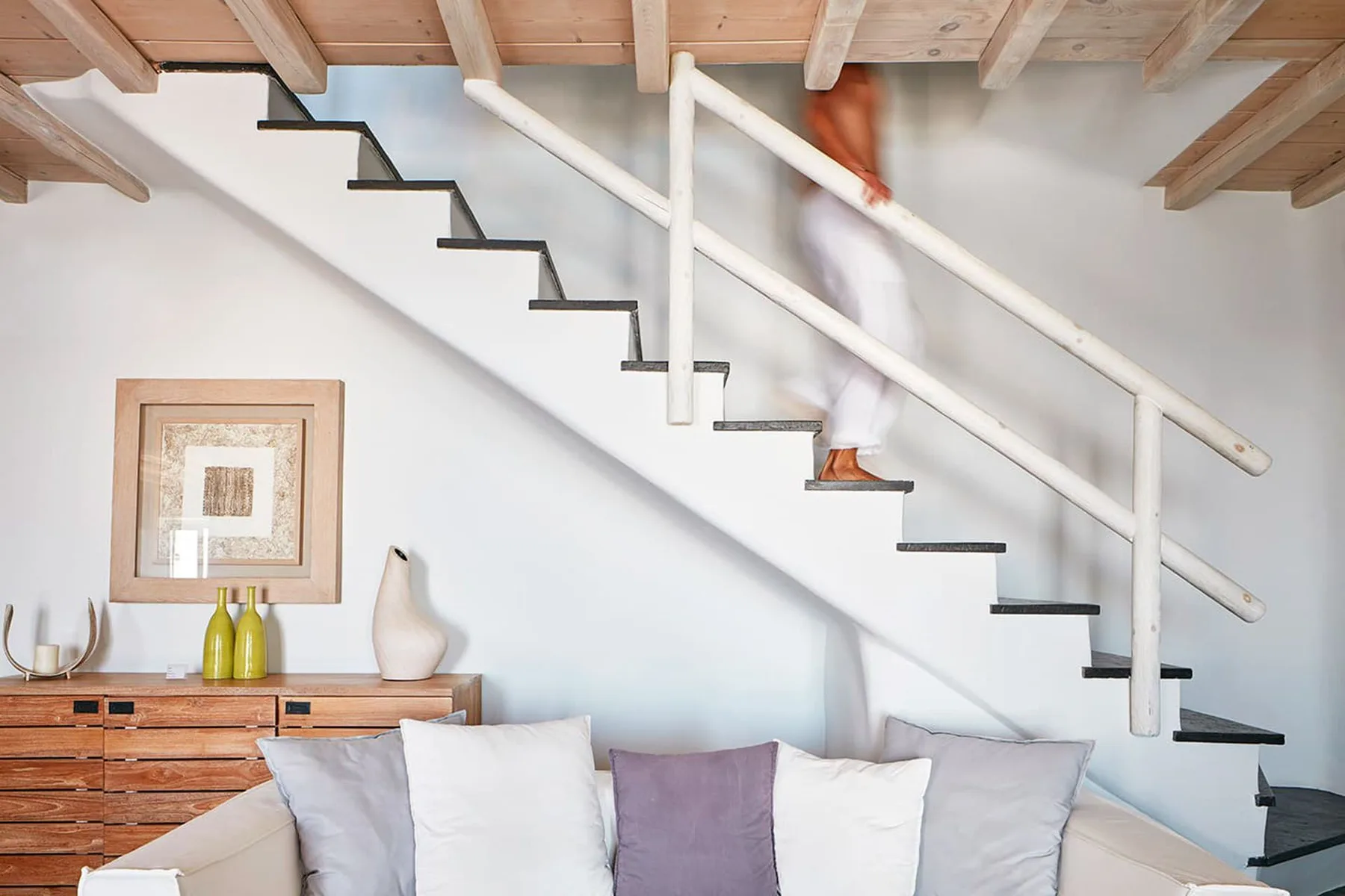 A living room with a staircase above a sofa and cushions.