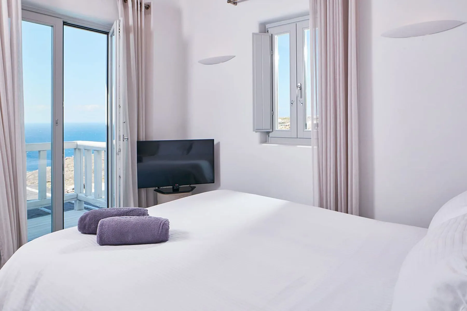 A bedroom with a bed, television, and sliding glass doors opening onto a balcony.