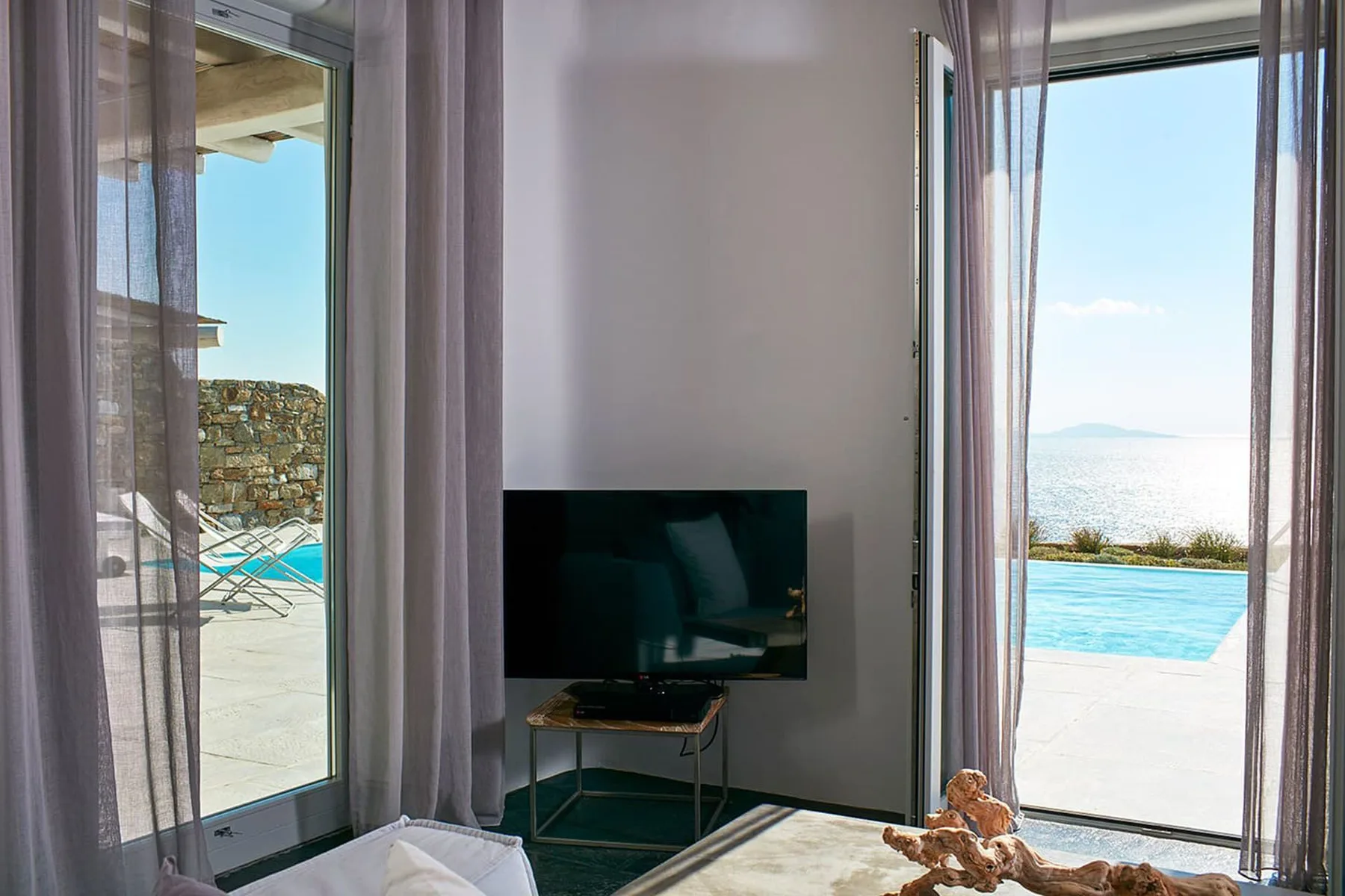 A bright living room opens onto a patio with a swimming pool and sea view.
