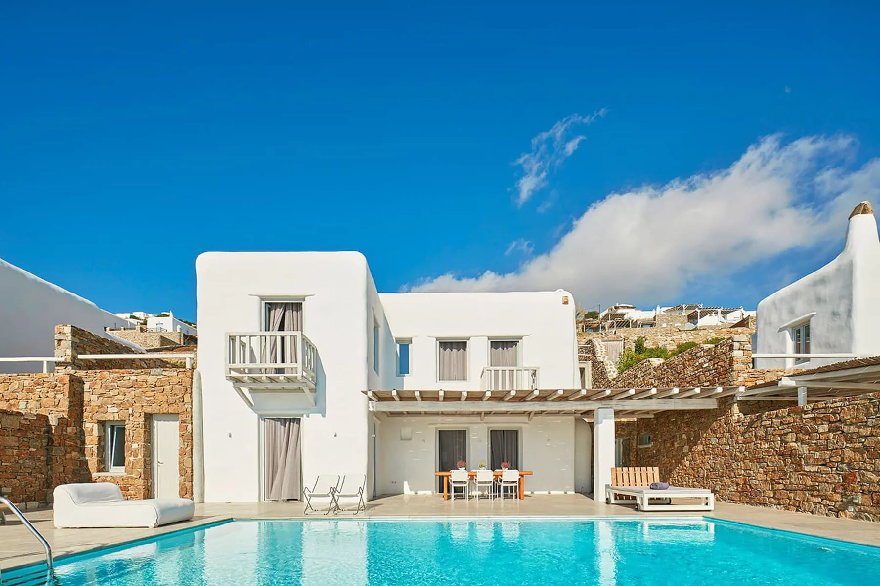A bright white villa overlooks a swimming pool beneath a clear blue sky.