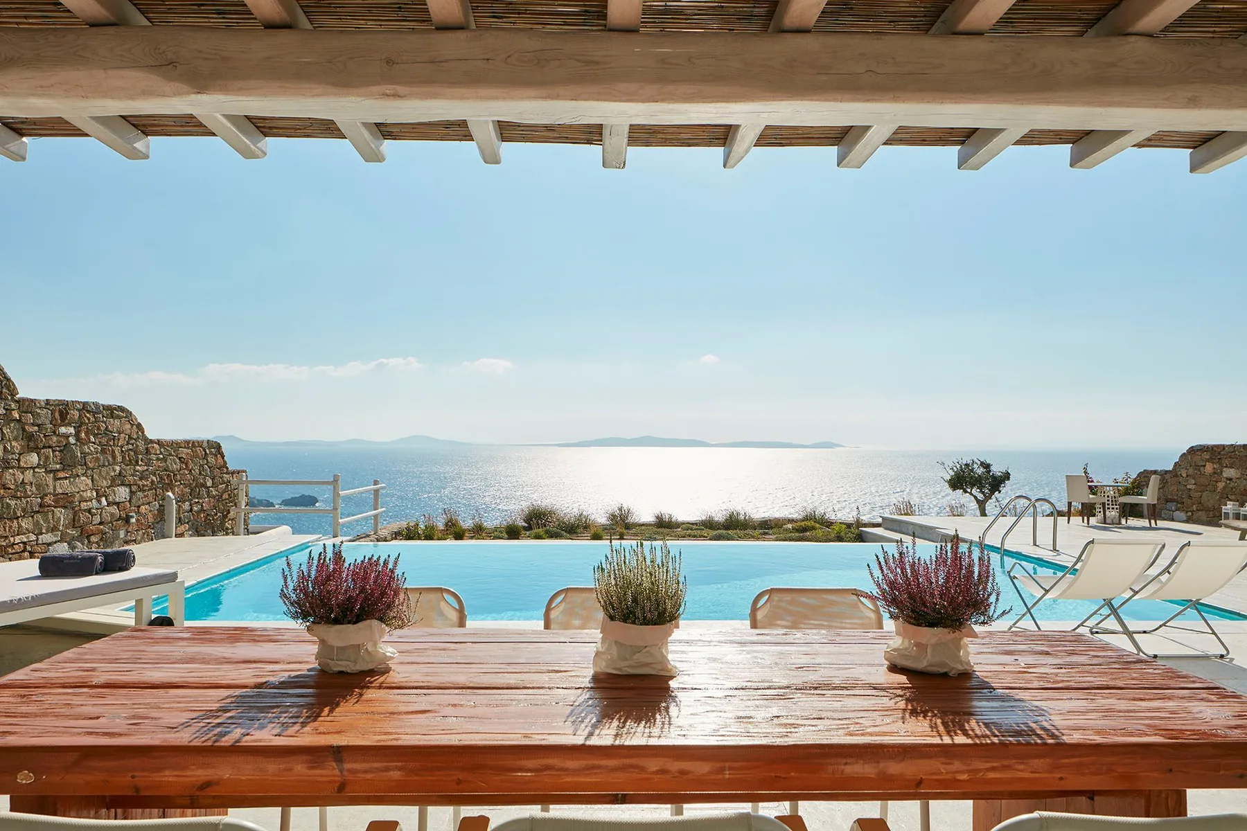 A terrace dining table overlooks a swimming pool and the sea.