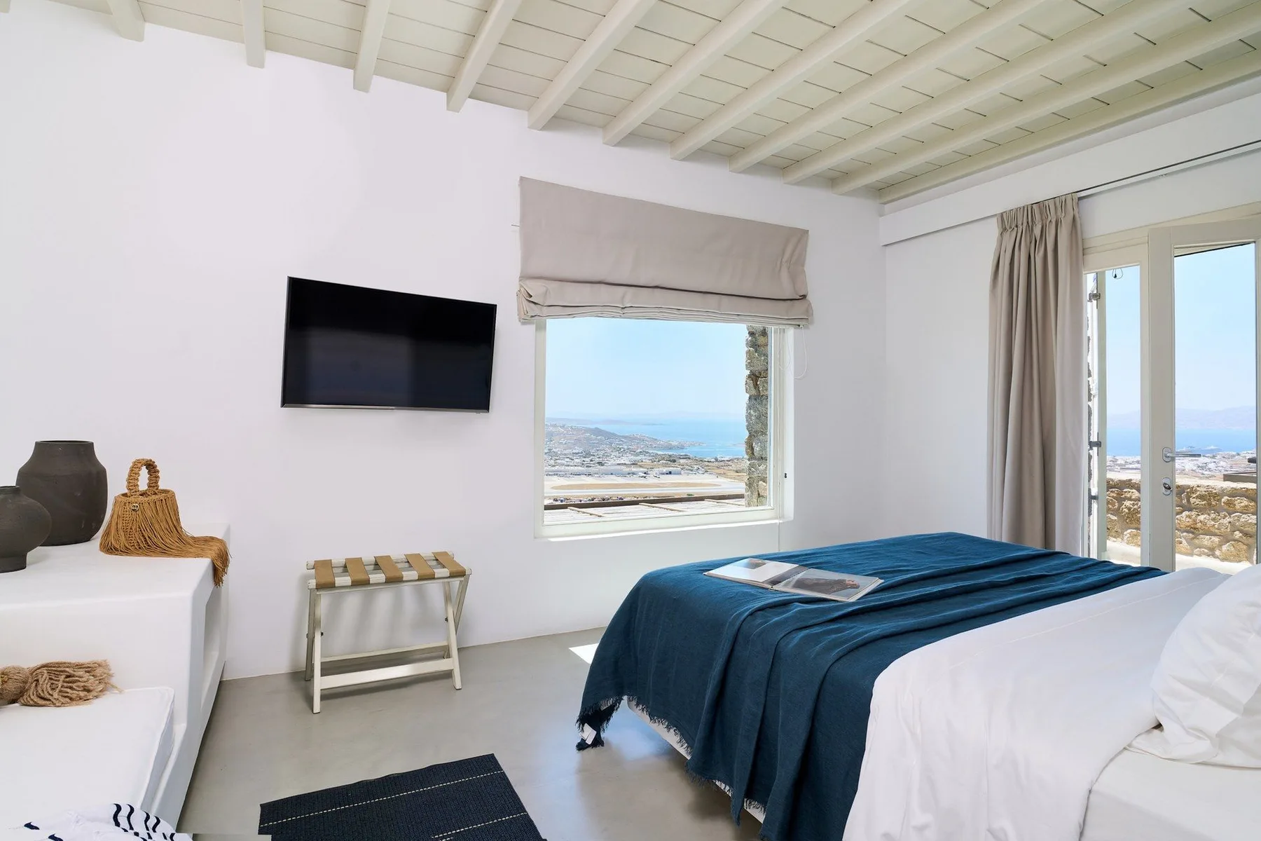 A bright bedroom has a bed with blue bedding and a view through the windows.