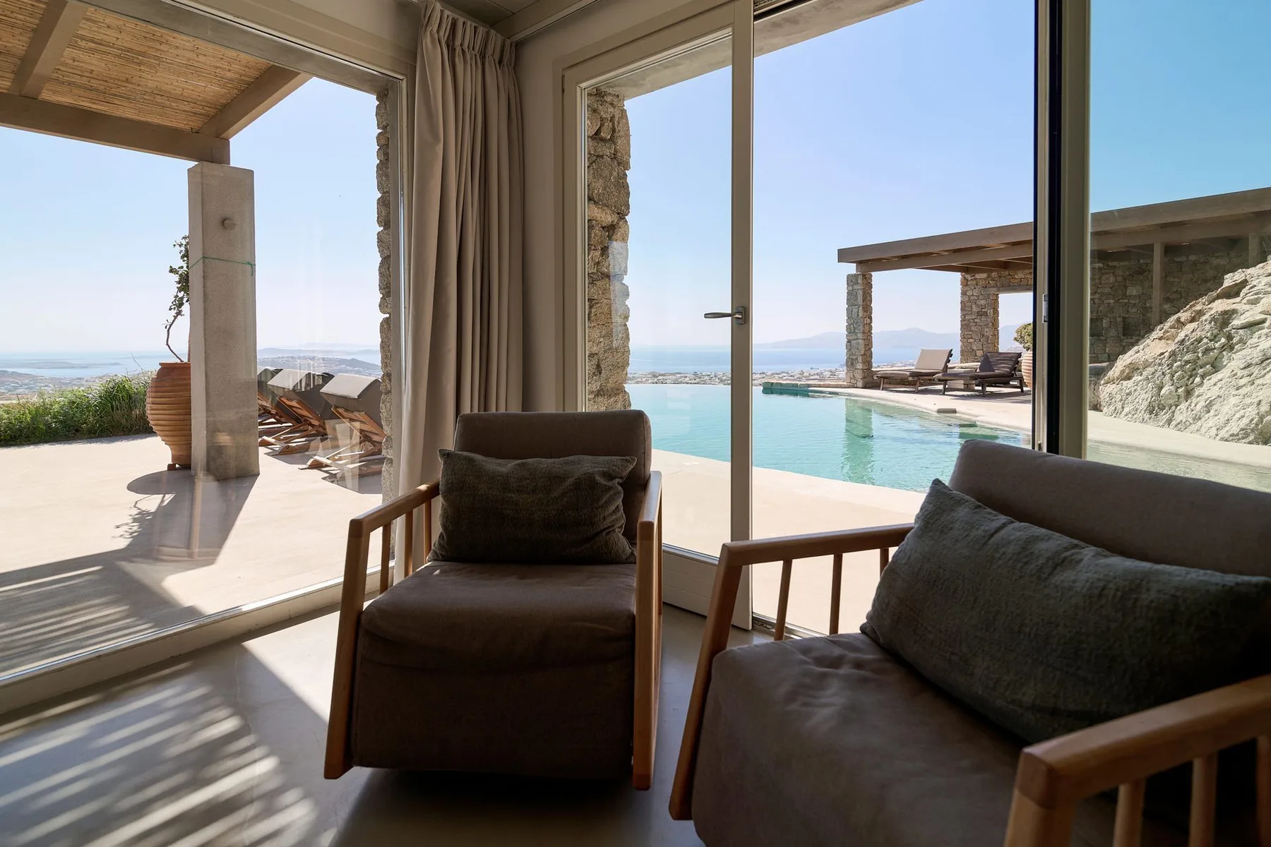 A bright living area opens onto a terrace with a swimming pool and distant sea views.