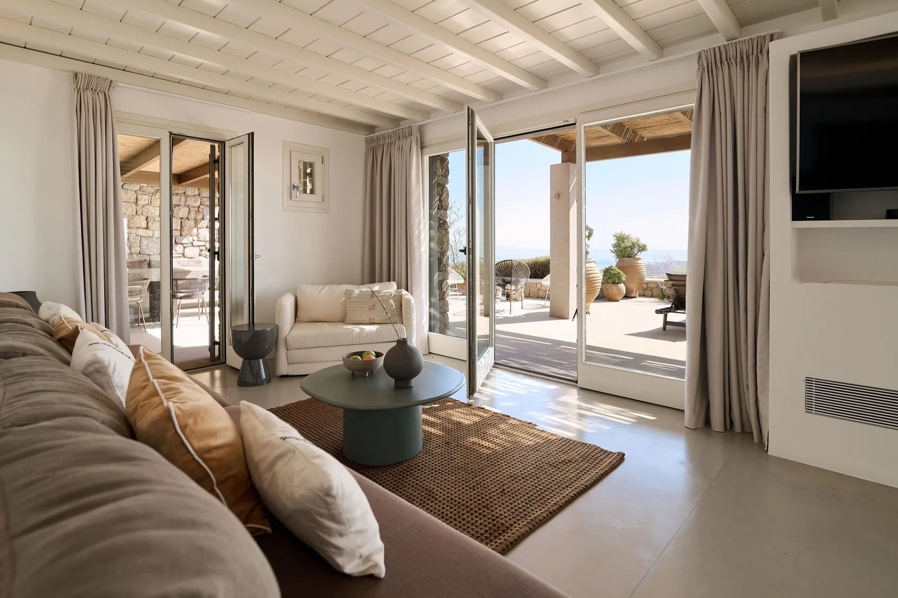 A bright living room with seating, a coffee table, and open doors to a sunny patio.