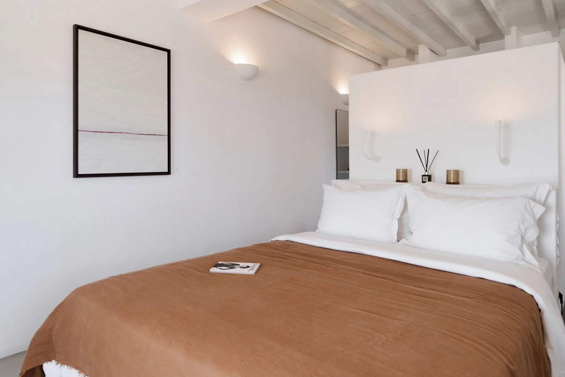 A bedroom with a neatly made bed, white linens, and a brown cover.