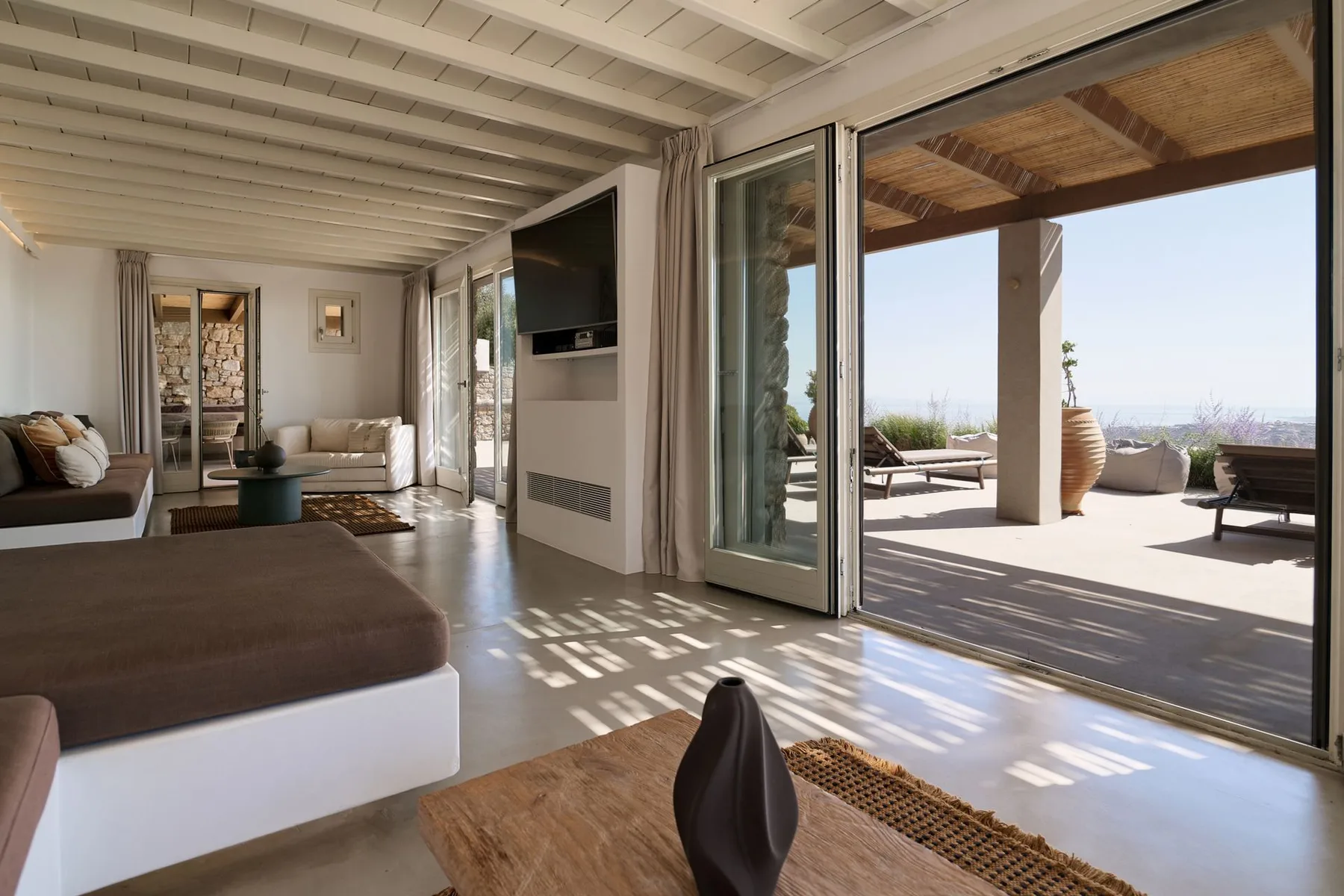 A bright living room opens onto a sunlit terrace through wide sliding glass doors.