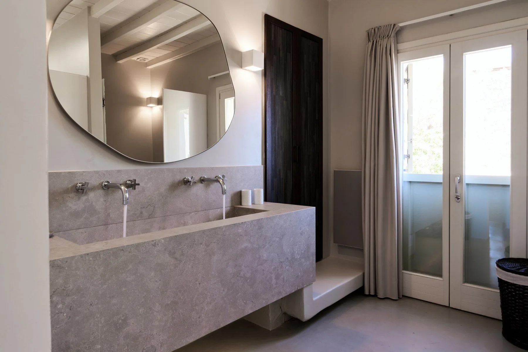 A bright bathroom with a long double vanity and glass doors opening to a balcony.