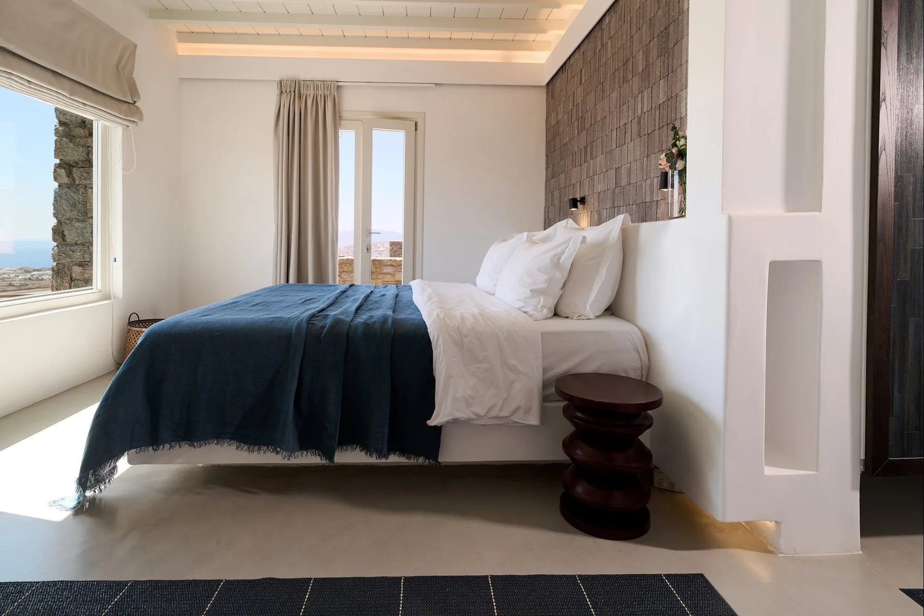 A bedroom with a bed dressed in white linens and a dark blue blanket.